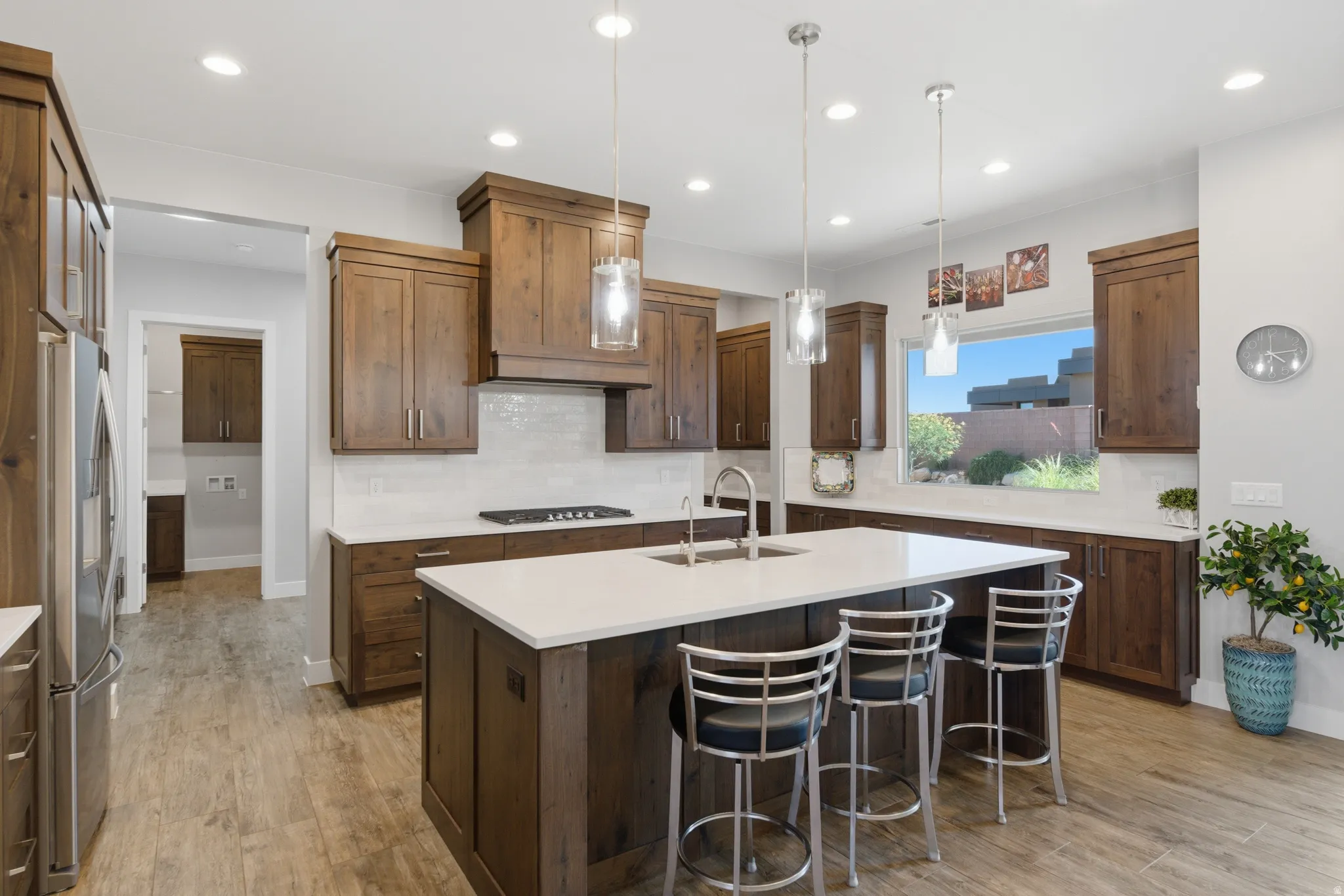 Spacious kitchen featuring an expansive center island with seating, wood-finish cabinetry, light-toned countertops, a tile backsplash, and wood-finish flooring