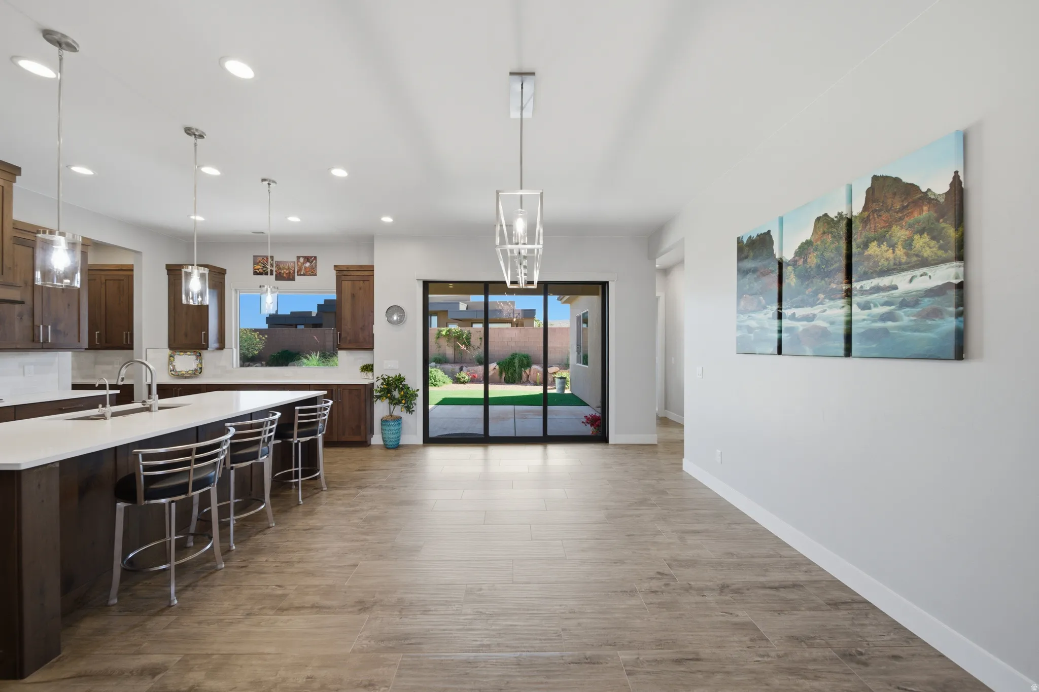 Open concept living area featuring wood-finish flooring, a kitchen island with seating, a sliding glass door to the backyard, recessed lighting, and pendant light fixtures