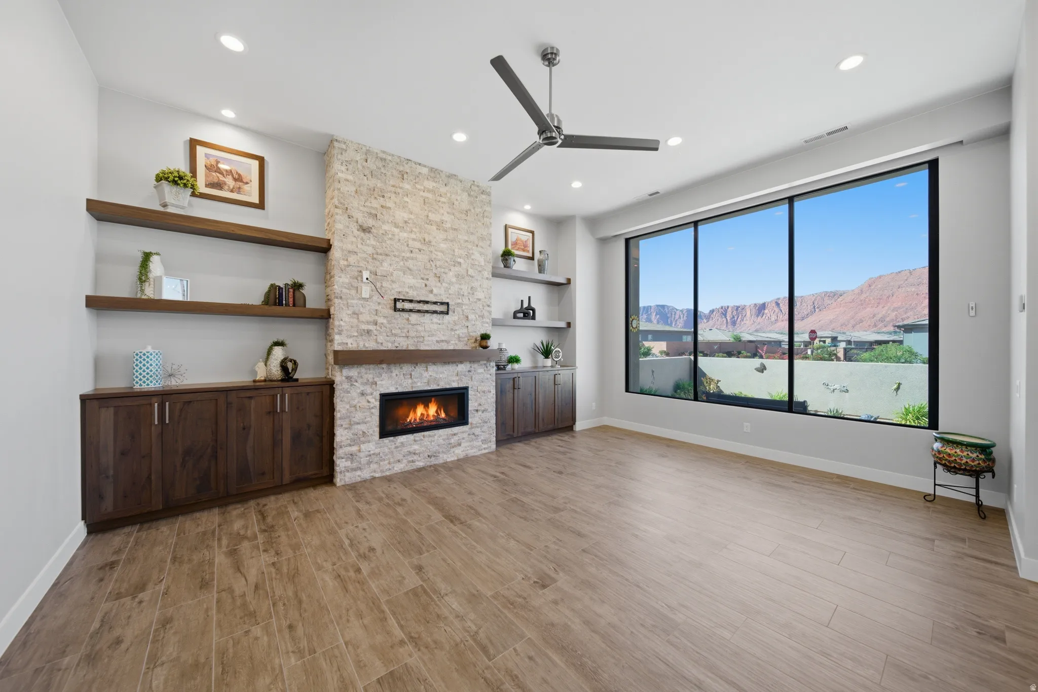 Spacious room featuring a stone-clad fireplace with a dark wood mantel, built-in cabinetry, and floating shelves