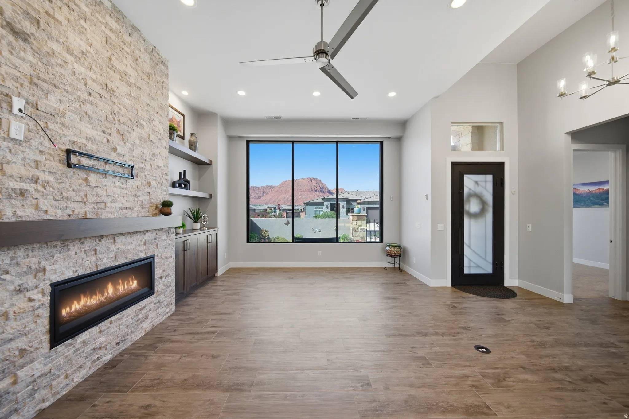 Spacious living area featuring a stacked stone fireplace, a contemporary ceiling fan, and large windows