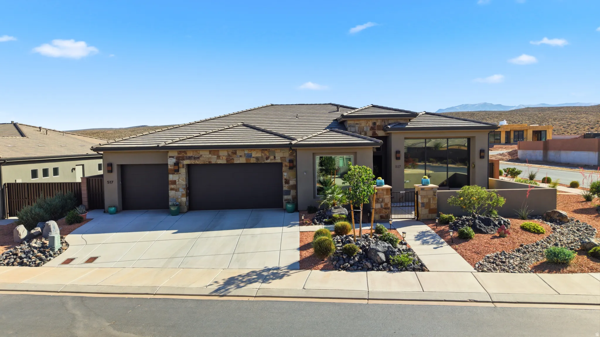 Contemporary single-story residence featuring a stone and stucco exterior, two-car garage, low-maintenance desert landscaping, a tiled roof, and a gated entry courtyard