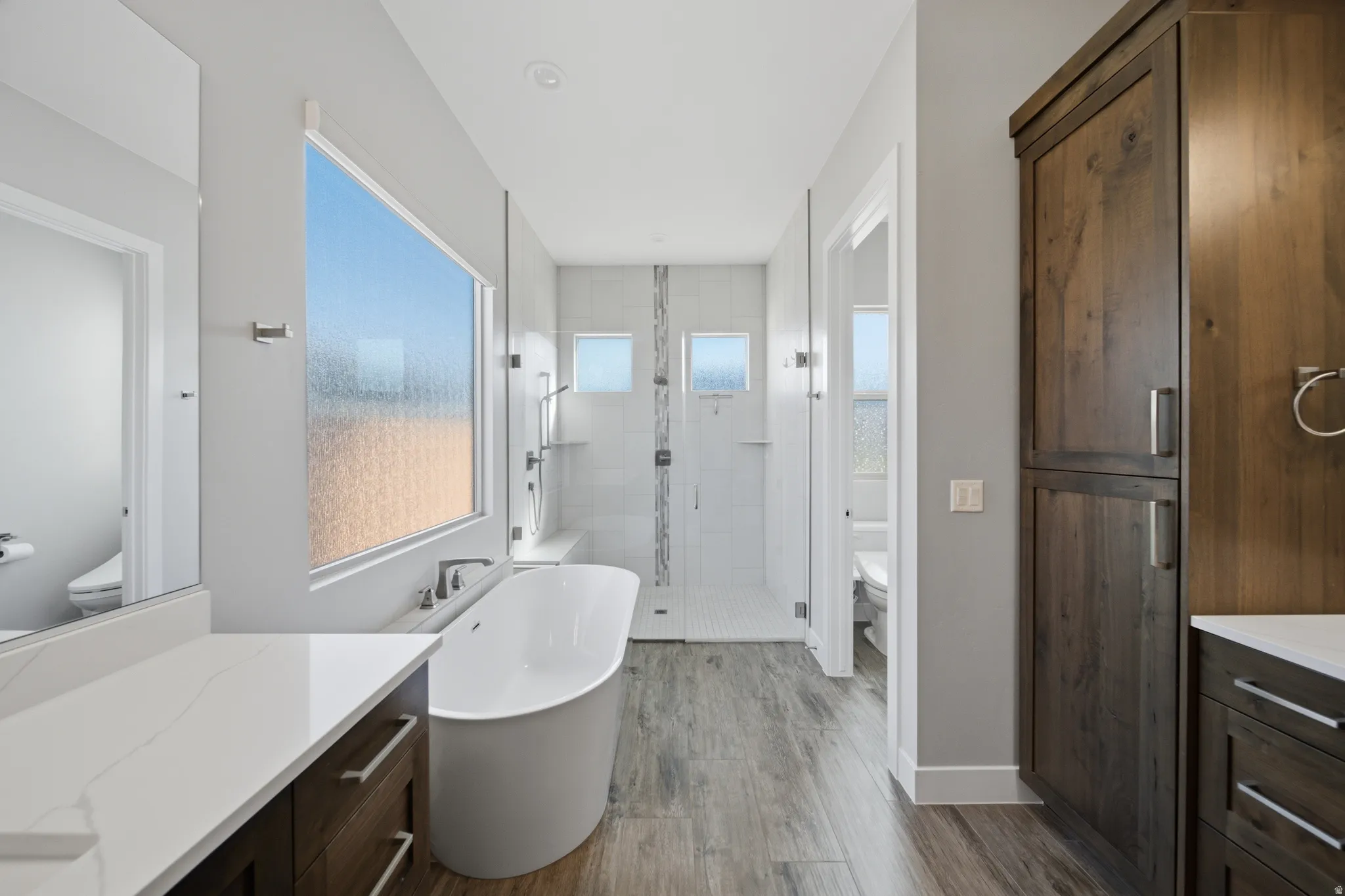 Freestanding soaking tub with a floor-mounted faucet, a frosted picture window, and wood-finish flooring