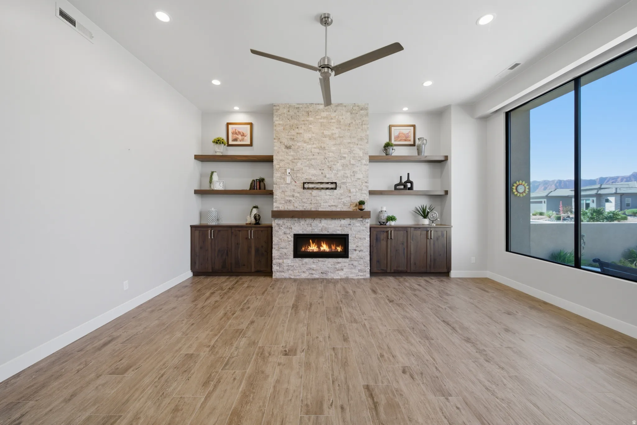 Living area featuring a stone-clad fireplace with a wood mantel, built-in shelving, recessed lighting, and a contemporary ceiling fan