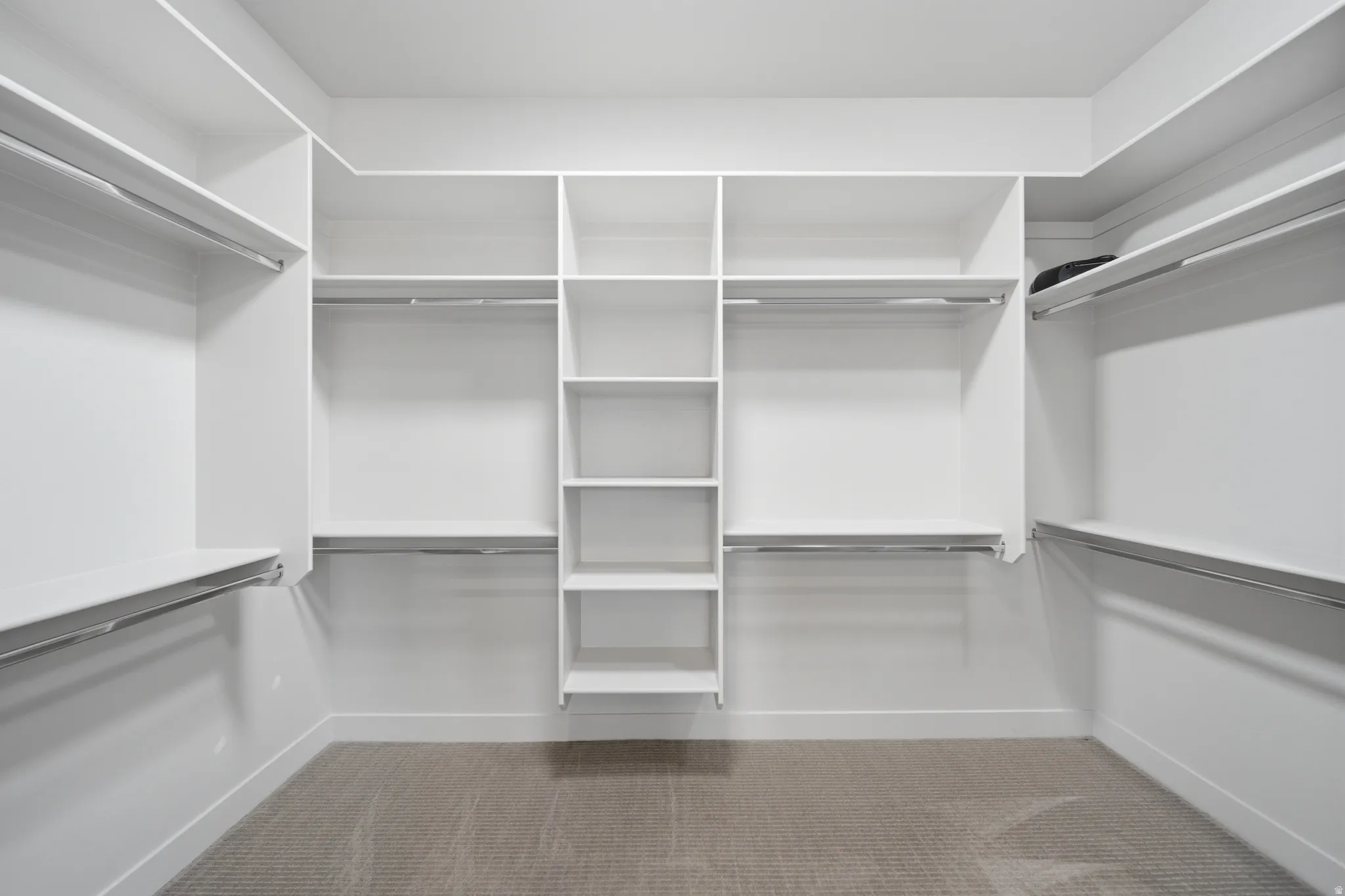 Walk-in closet featuring built-in white shelving, multiple hanging rods, and carpeted flooring