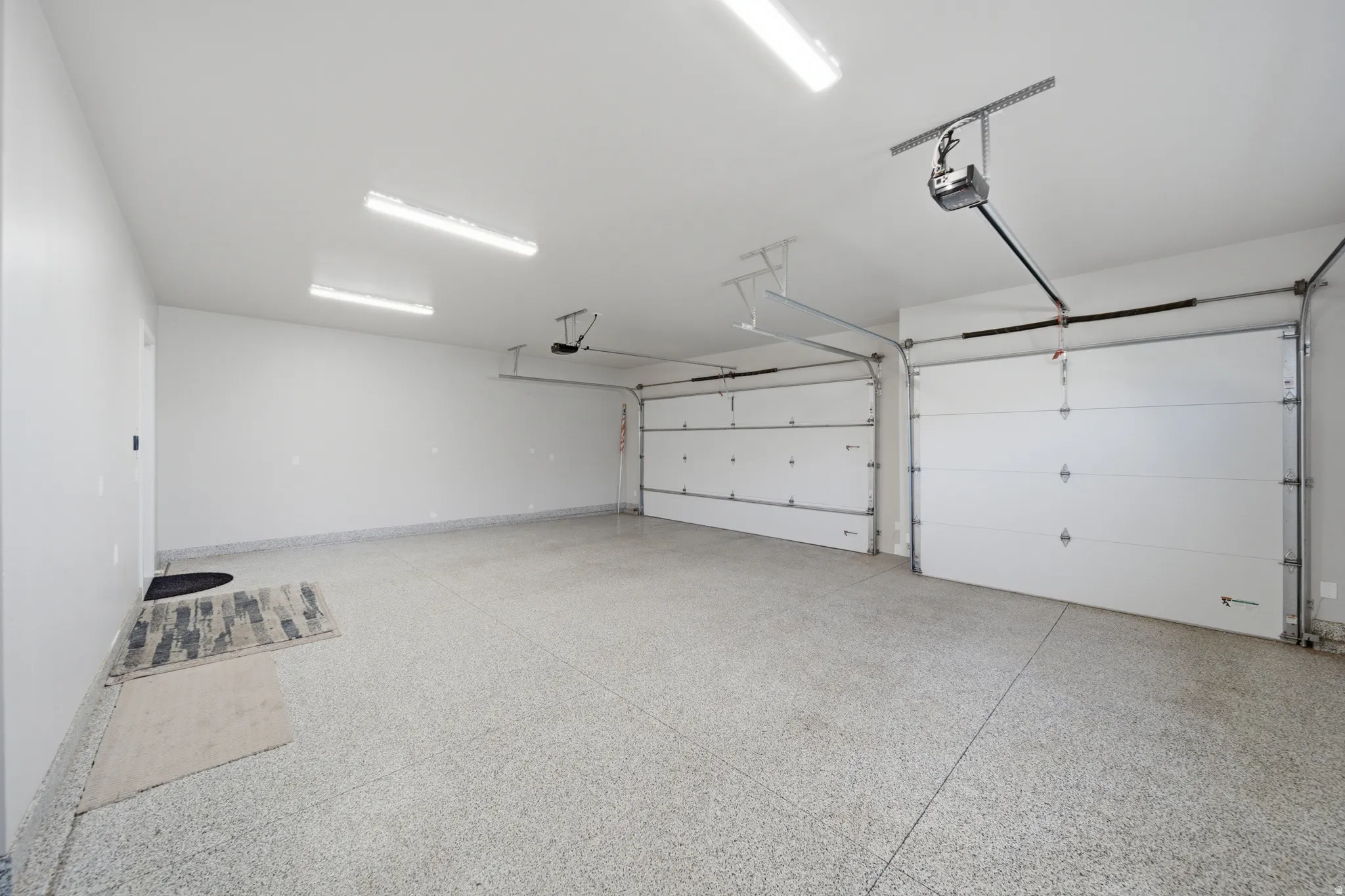 Spacious garage featuring two overhead doors, automatic openers, epoxy flooring, and ample overhead lighting