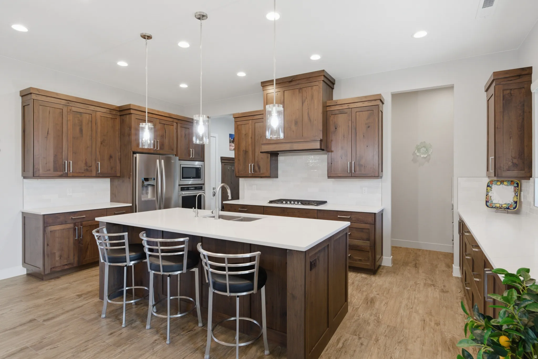 Kitchen featuring wood-finish cabinetry, white countertops, a central island with pendant lighting, stainless steel appliances, and wood-finish flooring