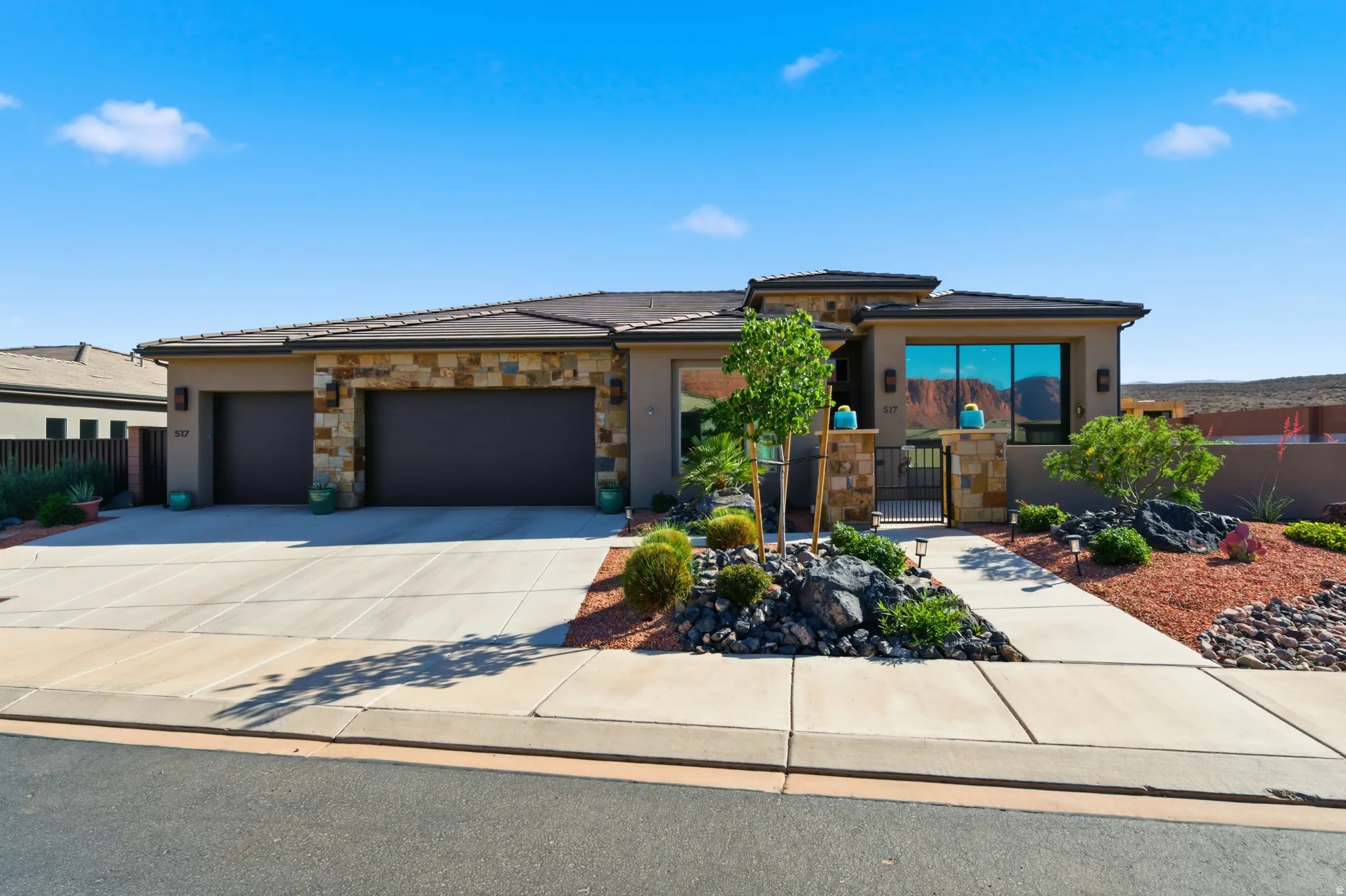 Contemporary stucco exterior featuring stone accents, a multi-car garage, and a gated entry leading to the main entrance