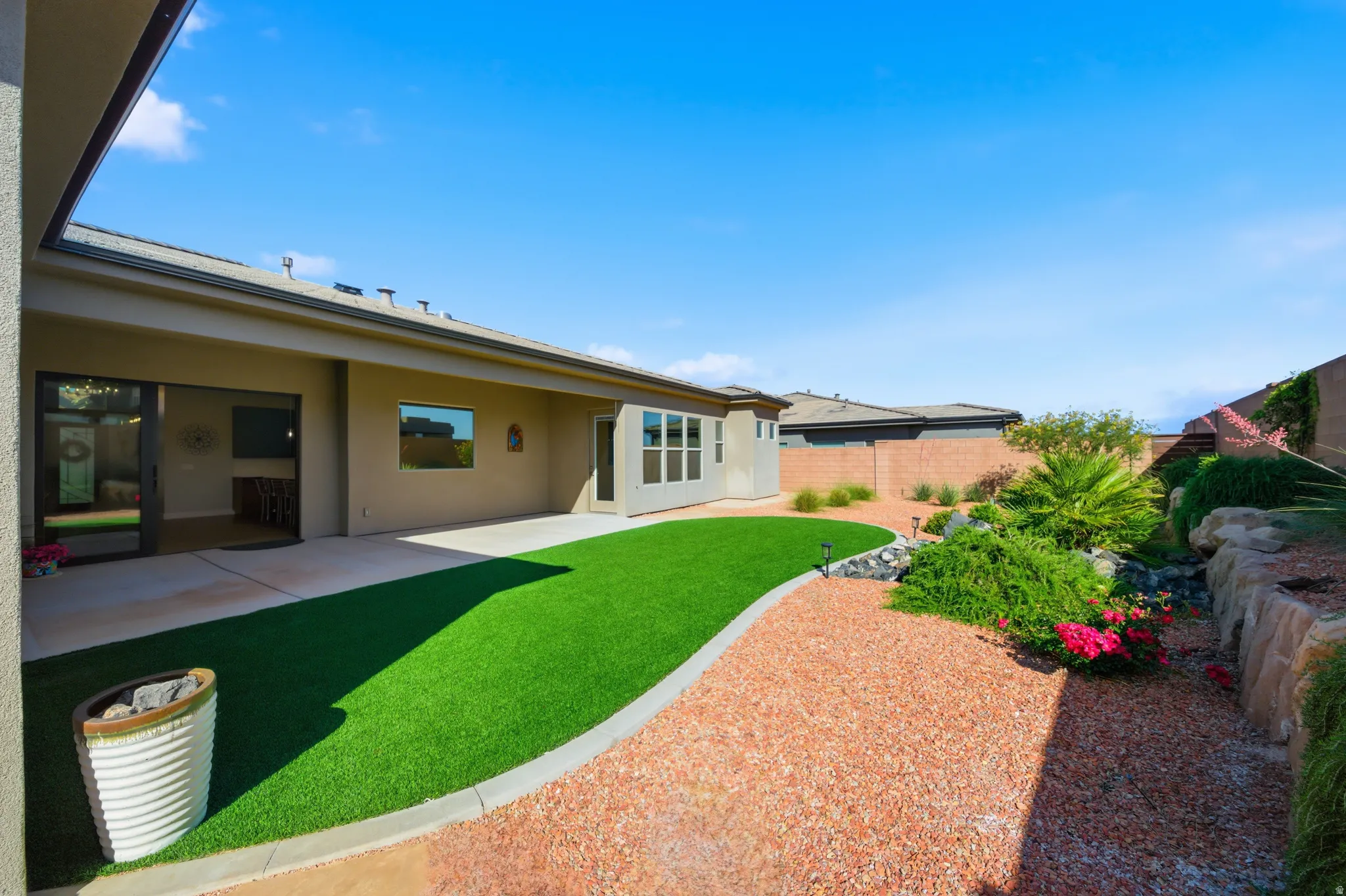 Expansive outdoor living area featuring a covered patio, artificial turf lawn, and desert landscaping with decorative rocks and mature plantings