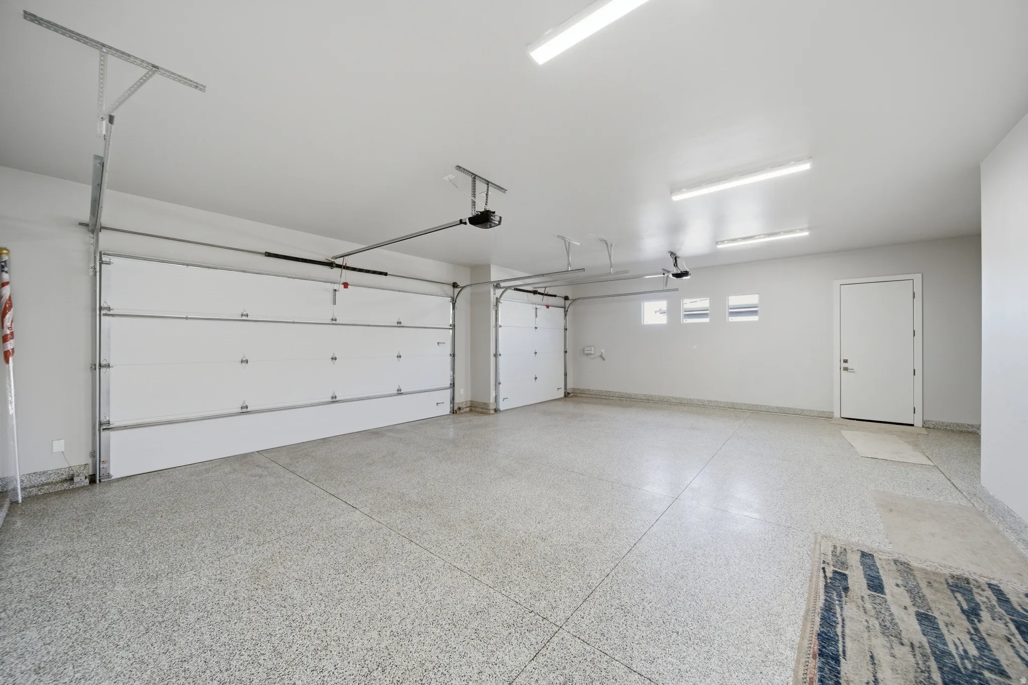 Spacious garage featuring a durable epoxy floor, white sectional garage doors, and multiple ceiling-mounted light fixtures