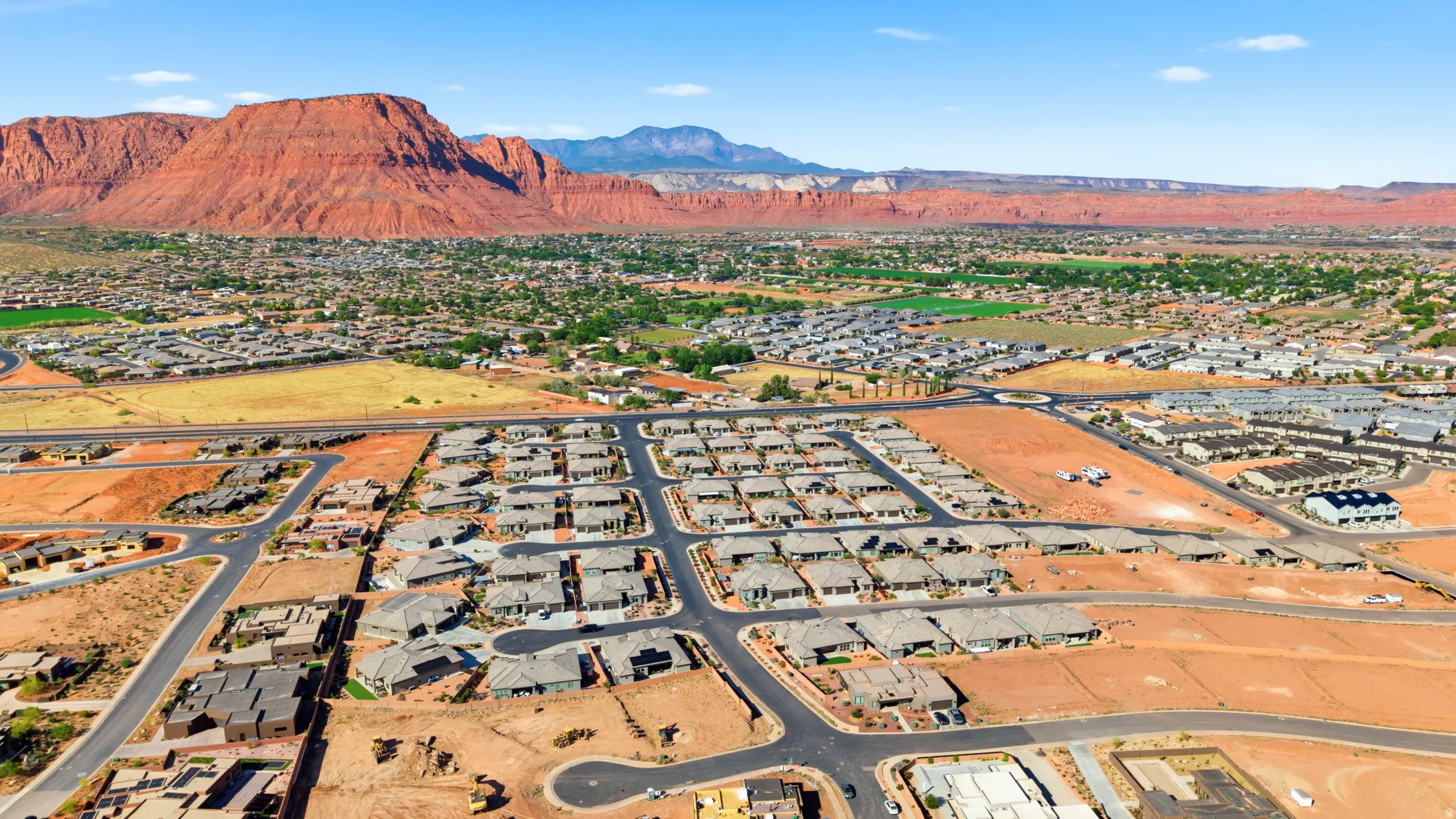 Expansive aerial perspective showcasing a residential development with numerous single-story homes, surrounded by natural red rock formations and distant mountains