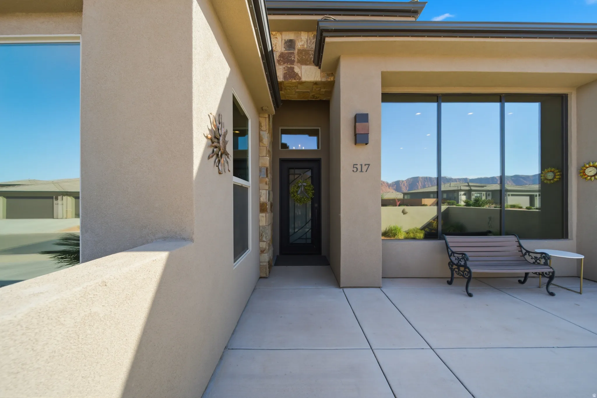 Contemporary stucco exterior featuring a stone accent wall, large picture windows, a dark framed entry door with glass inserts, and a built-in outdoor sconce