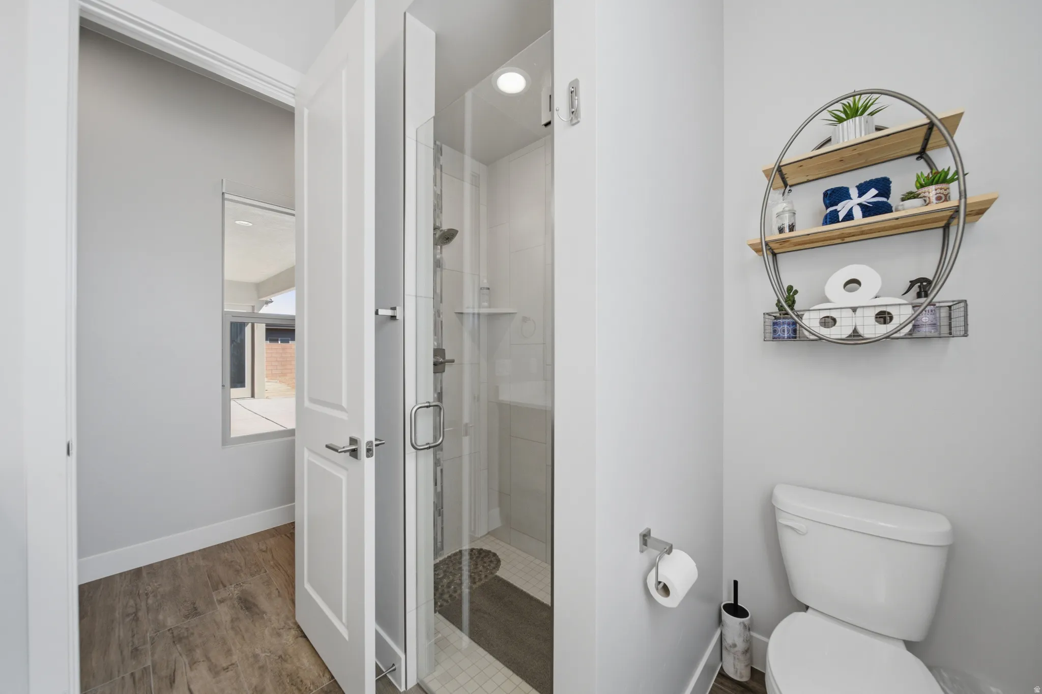 Bathroom featuring a glass-enclosed shower with a pebble-style floor, wood-finish flooring, and a window
