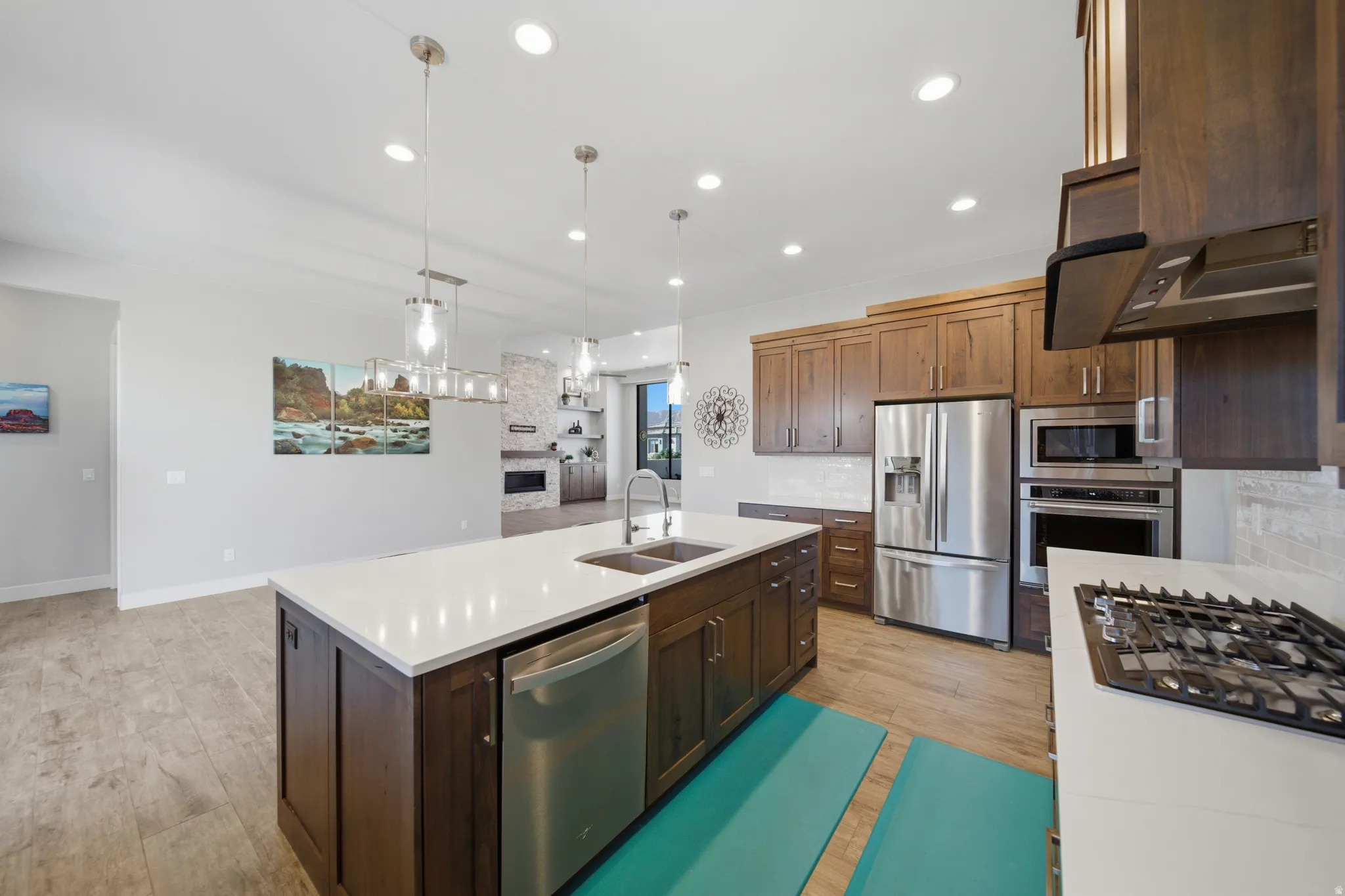 Expansive kitchen featuring a large island with a dual-basin sink, quartz countertops, stainless steel appliances, wood-finish cabinetry, and recessed lighting