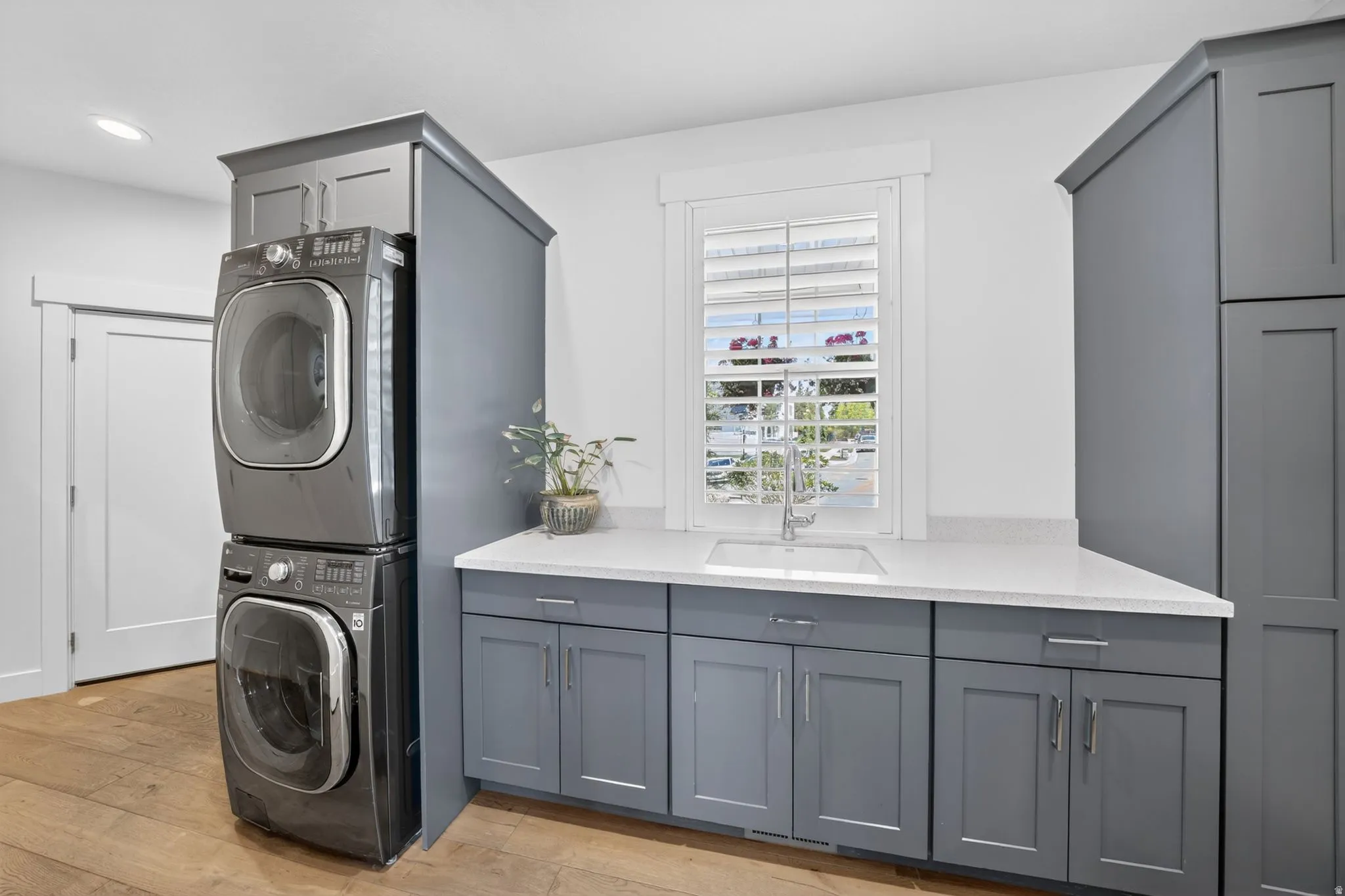 Functional laundry area featuring a built-in sink, white countertop, window with plantation shutters, and extensive shaker-style cabinetry