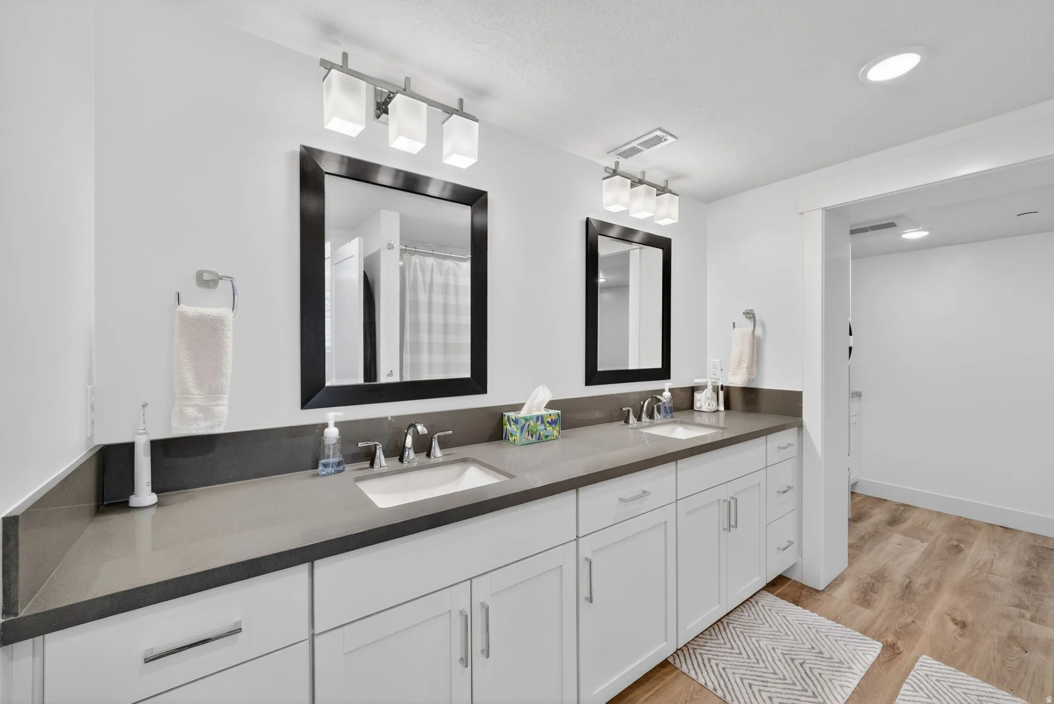 Mother in Law - Dual vanity featuring solid surface countertops, white cabinetry, undermount sinks, and wood-finish flooring