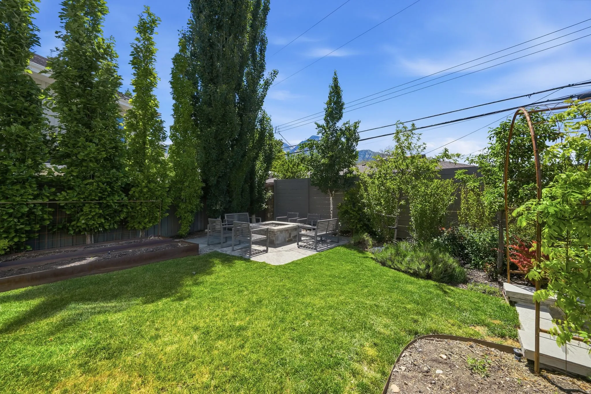 Expansive backyard featuring a stone patio with a built-in fire pit, surrounded by mature trees providing natural screening