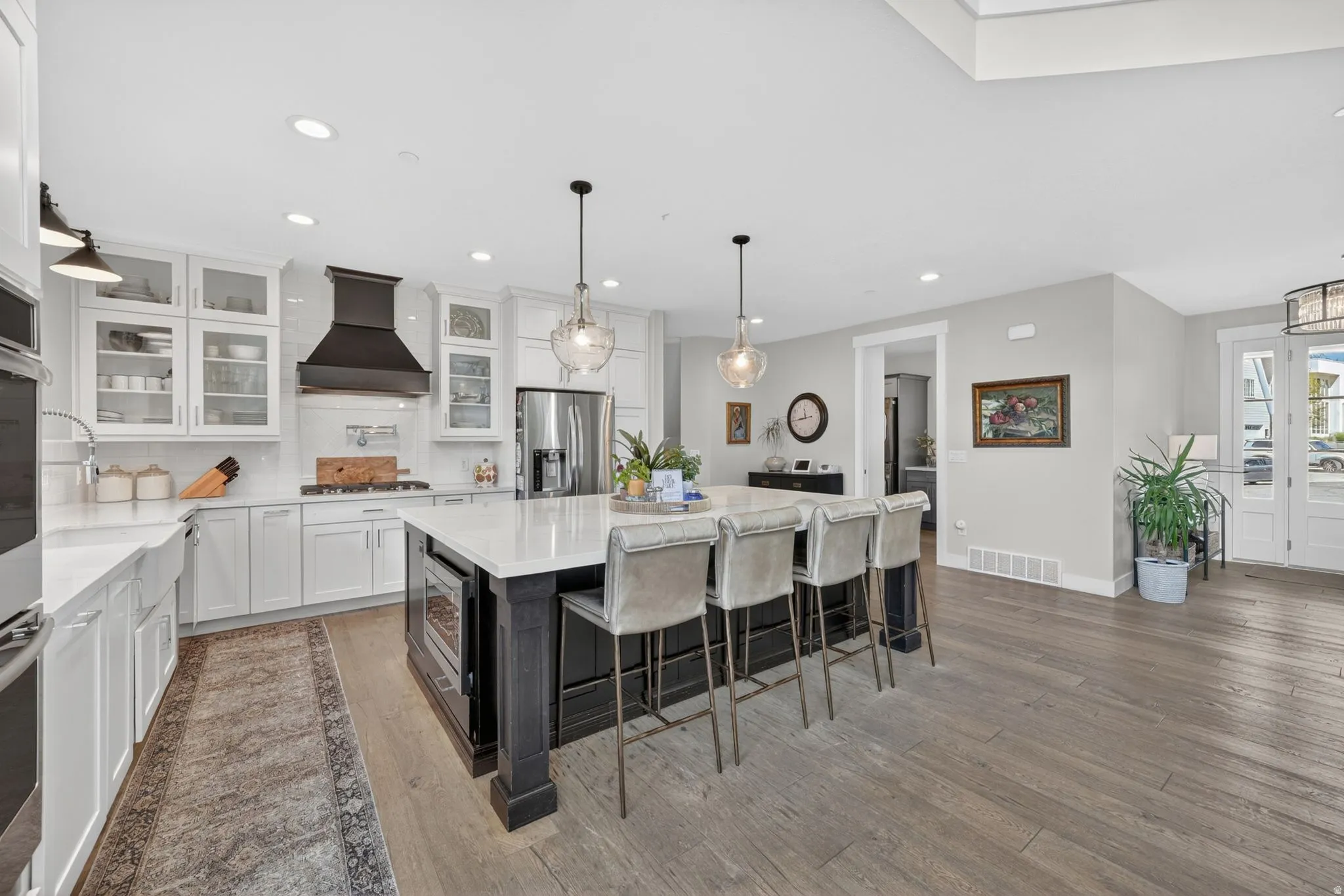 Gourmet kitchen with a large central island, white shaker cabinetry, stainless steel appliances, and wood-finish flooring