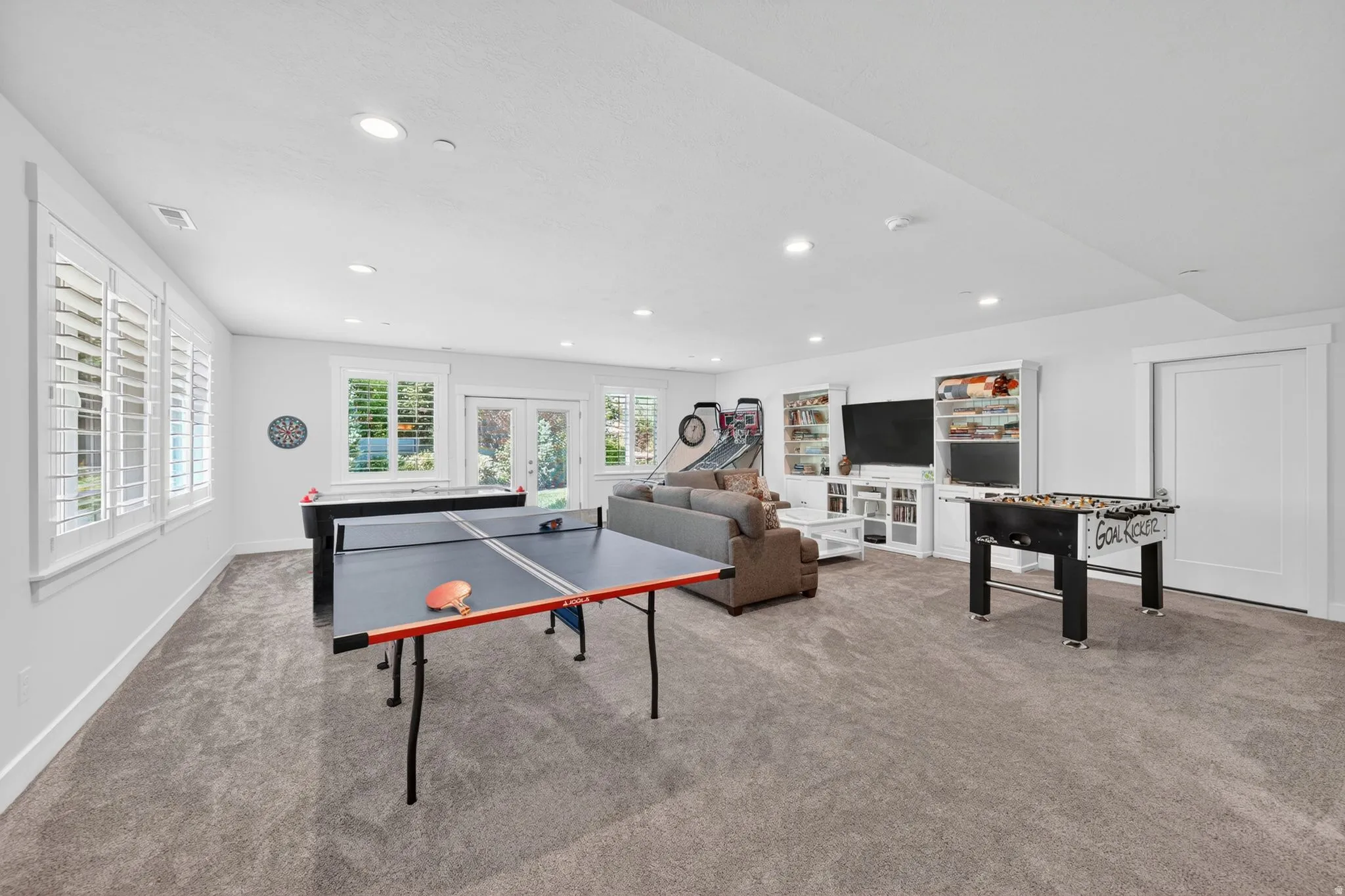 Expansive carpeted recreation room featuring white walls and recessed lighting
