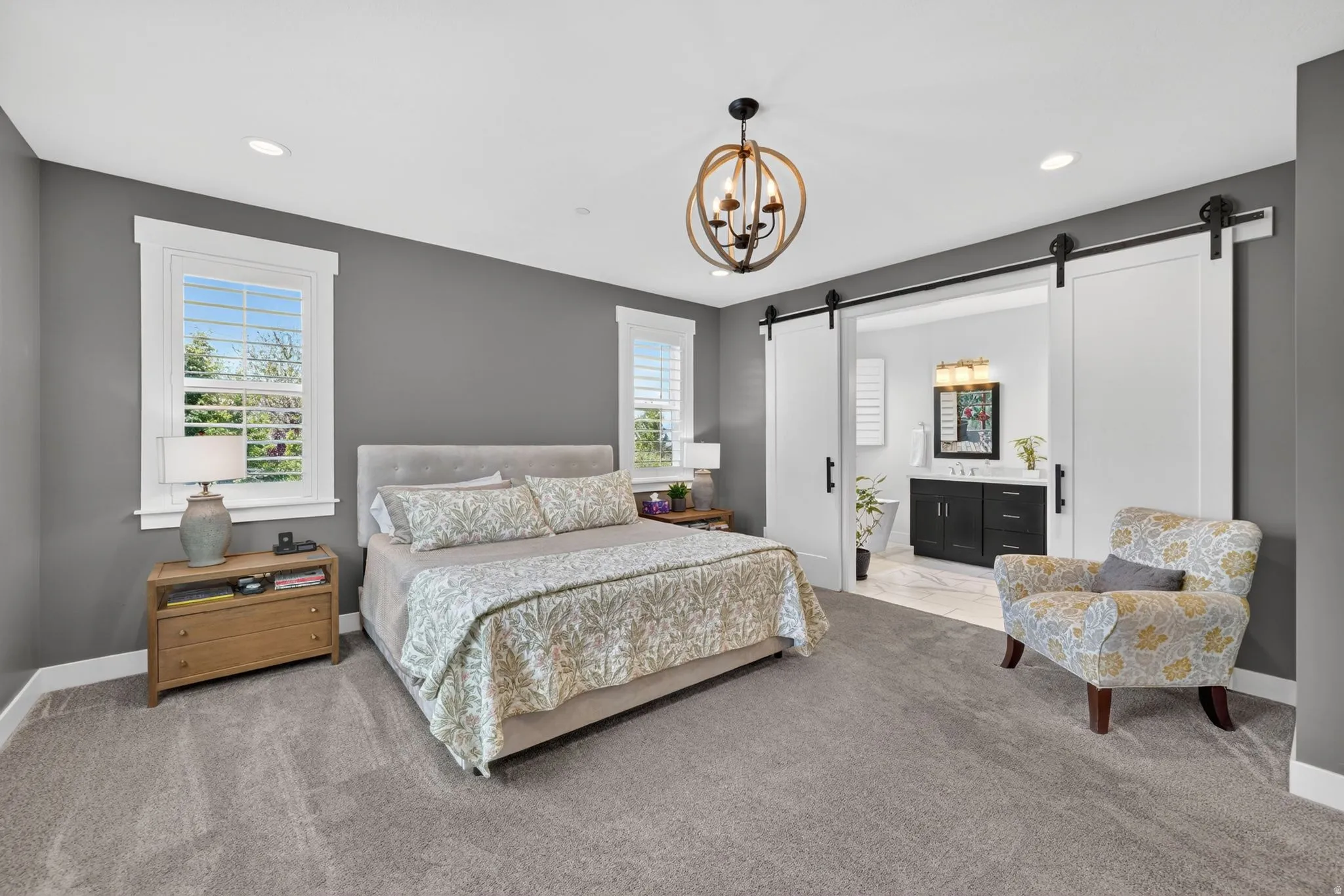 Spacious room featuring gray carpet flooring, white trim windows with louvered shutters, and a contemporary chandelier
