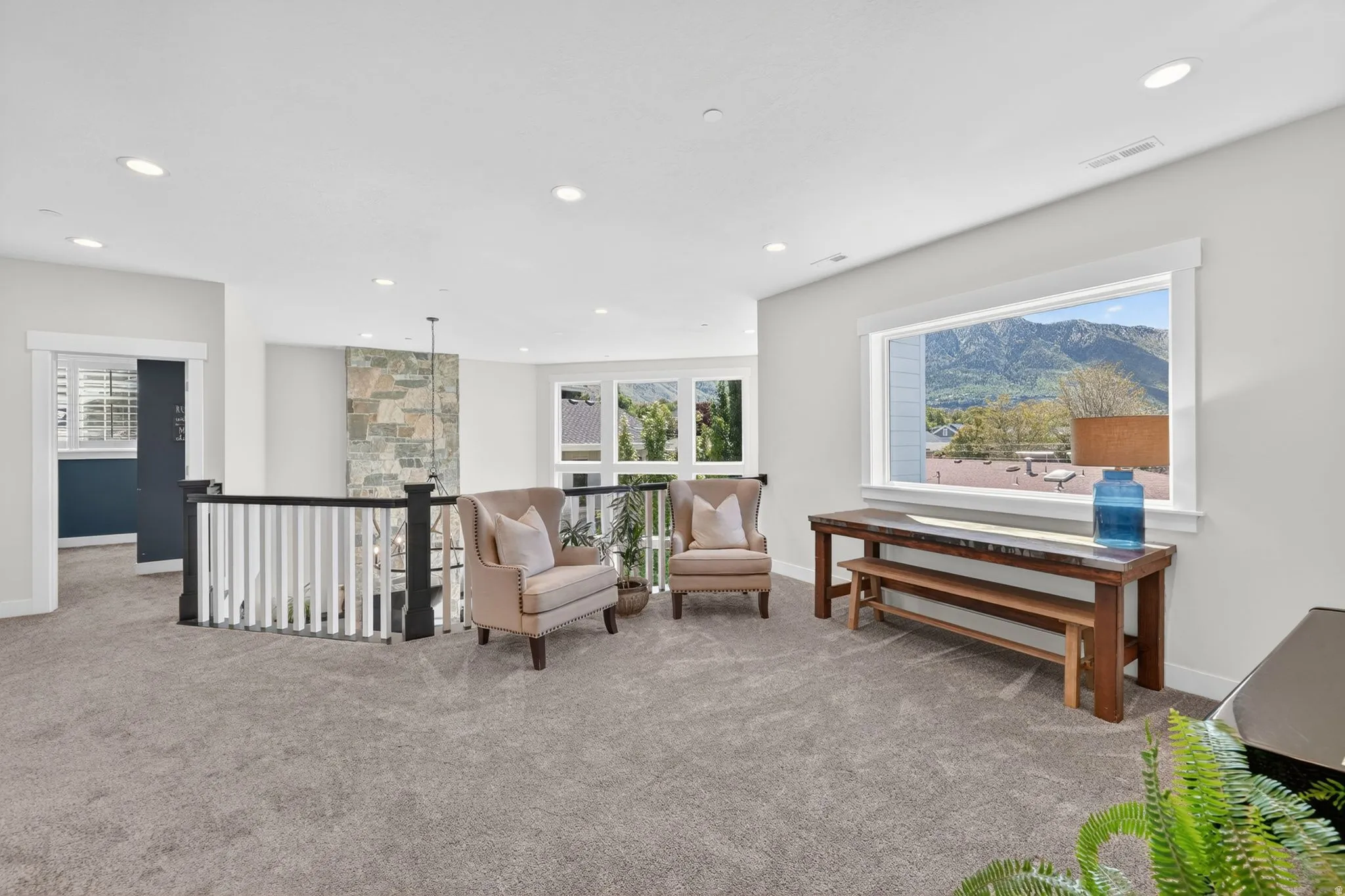Spacious carpeted upper level featuring a stone accent wall, recessed lighting, and white railings with dark wood newel posts