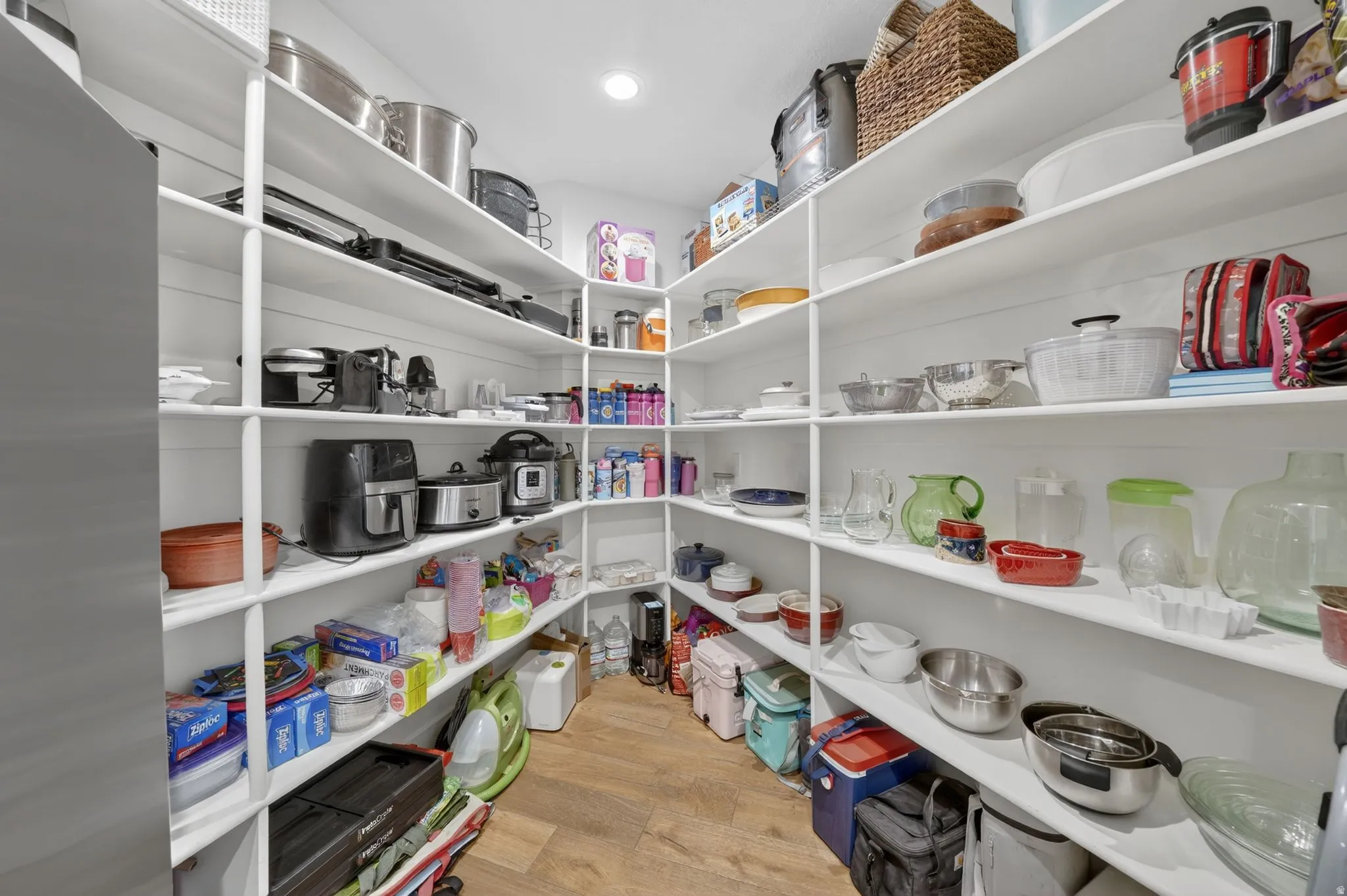Spacious pantry featuring extensive built-in shelving, durable wood-finish flooring, and recessed ceiling lighting
