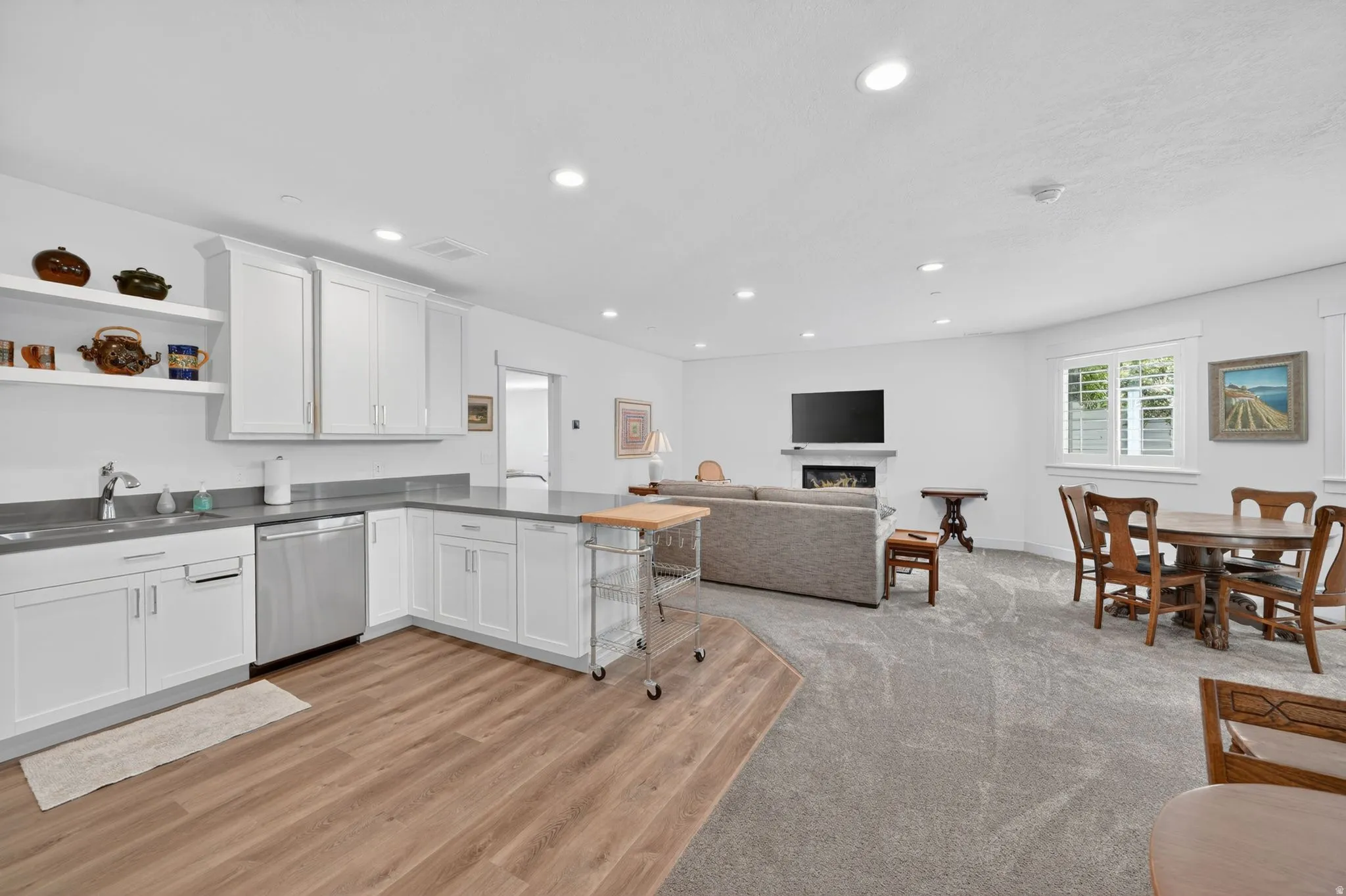 Mother in Law - Open-concept living area featuring a kitchen with white cabinetry and dark countertops, wood-finish flooring, recessed lighting, and a fireplace with a television above