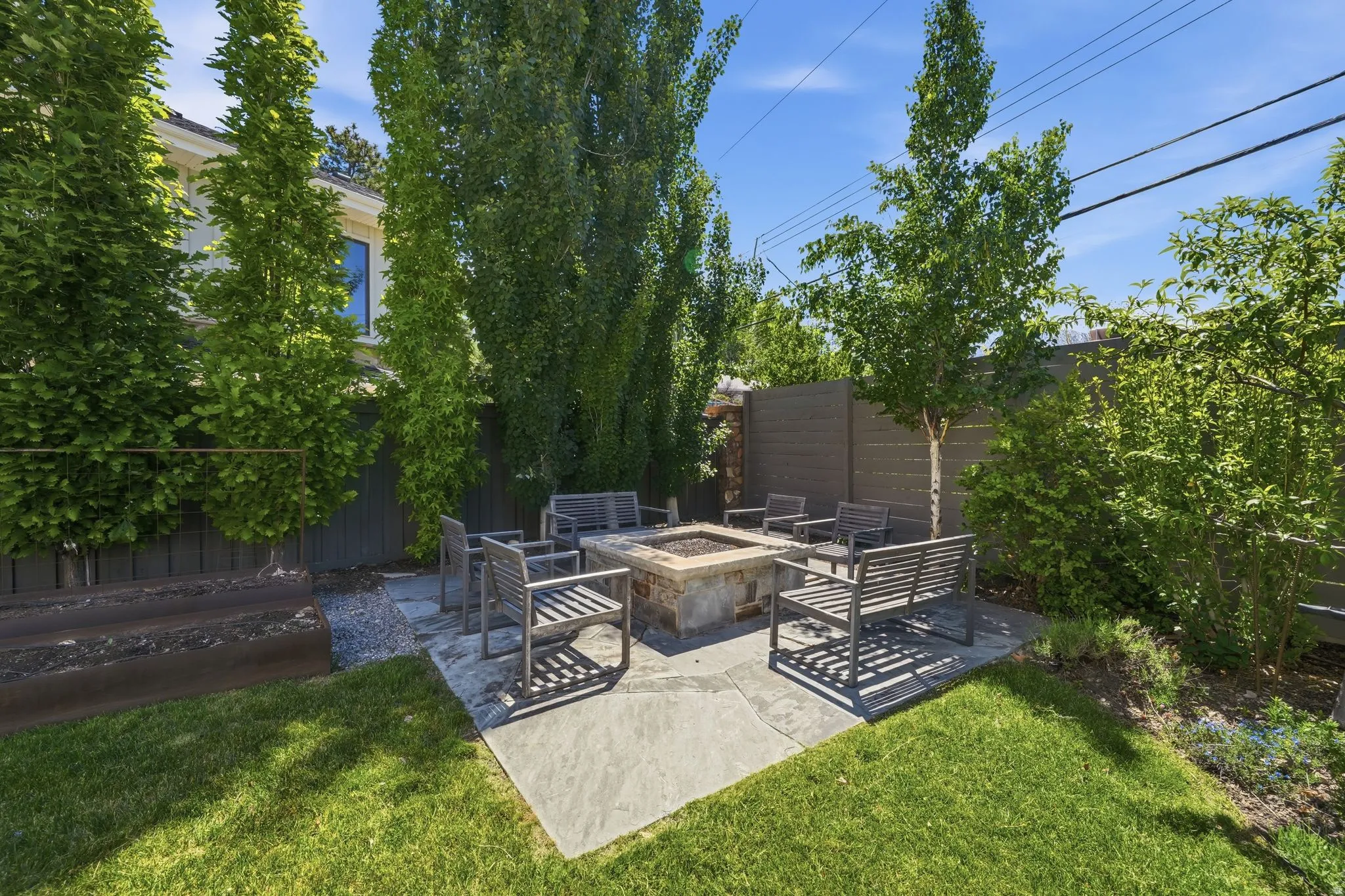 Expansive backyard featuring a stone-clad fire pit, surrounding stone patio, and a privacy fence