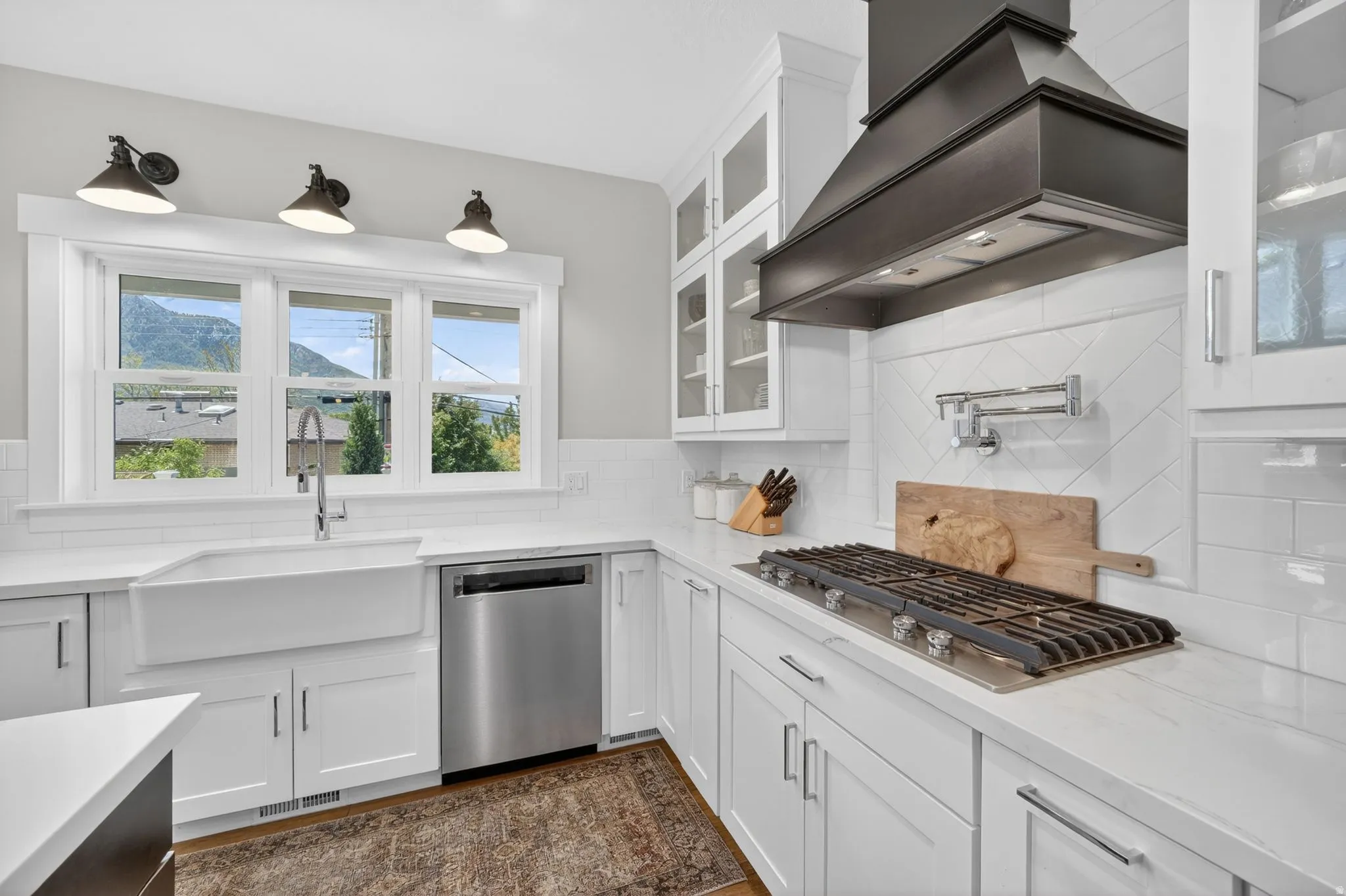 Kitchen featuring white cabinetry, integrated gas range, pot filler, stainless steel dishwasher, and a farmhouse sink