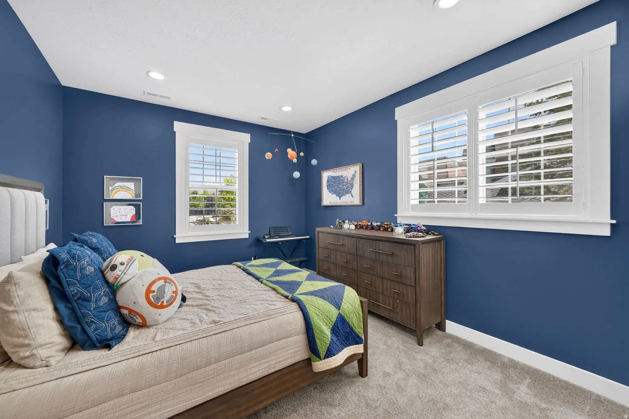 Spacious bedroom featuring dual windows with white plantation shutters, rich blue wall paint, and recessed ceiling lighting