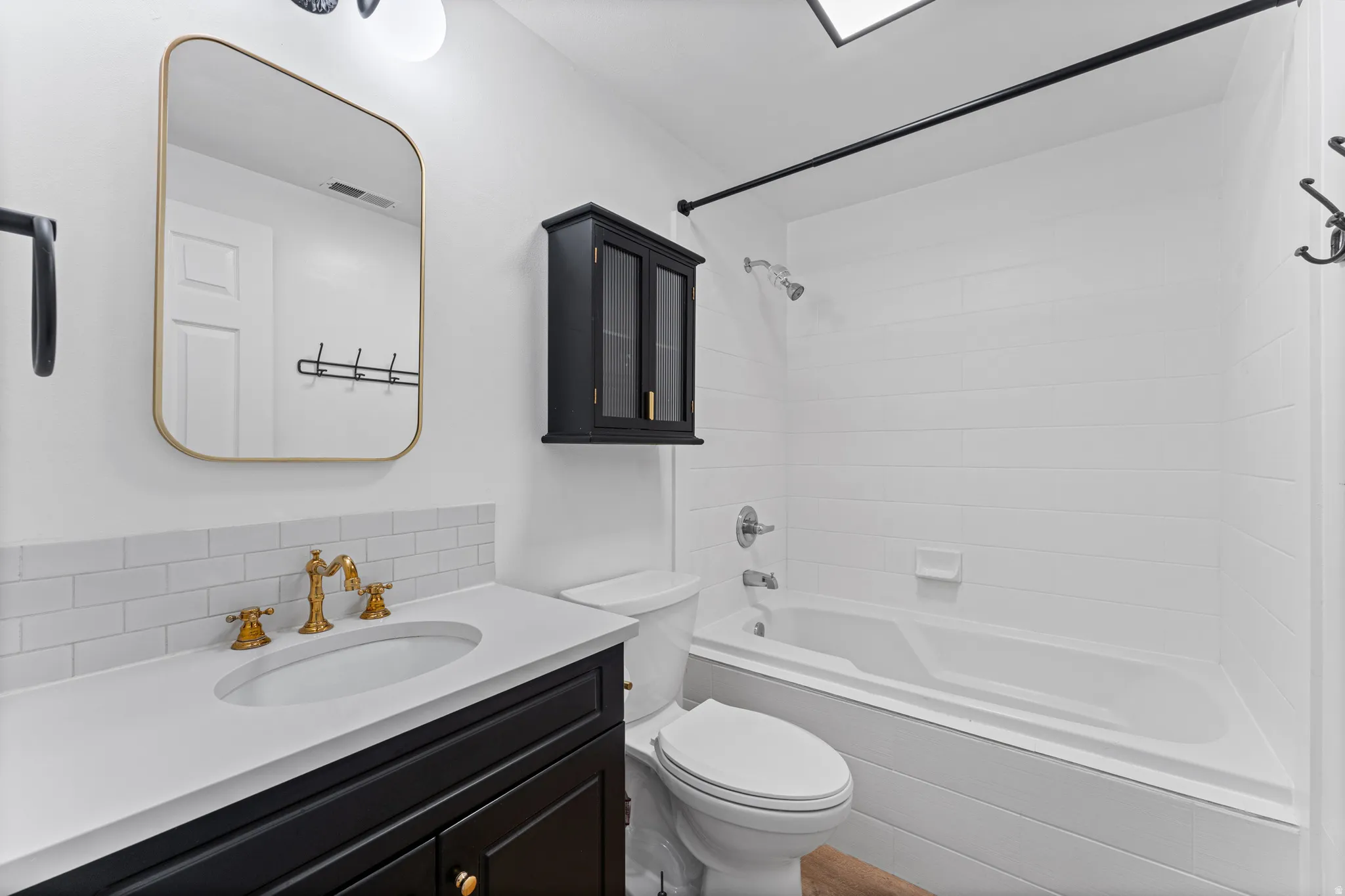 Bathroom featuring a white subway tile backsplash, a dark wood-finish vanity with a white countertop, a drop-in sink with a brass-finish faucet, and a combination tub and shower with white subway tile surround