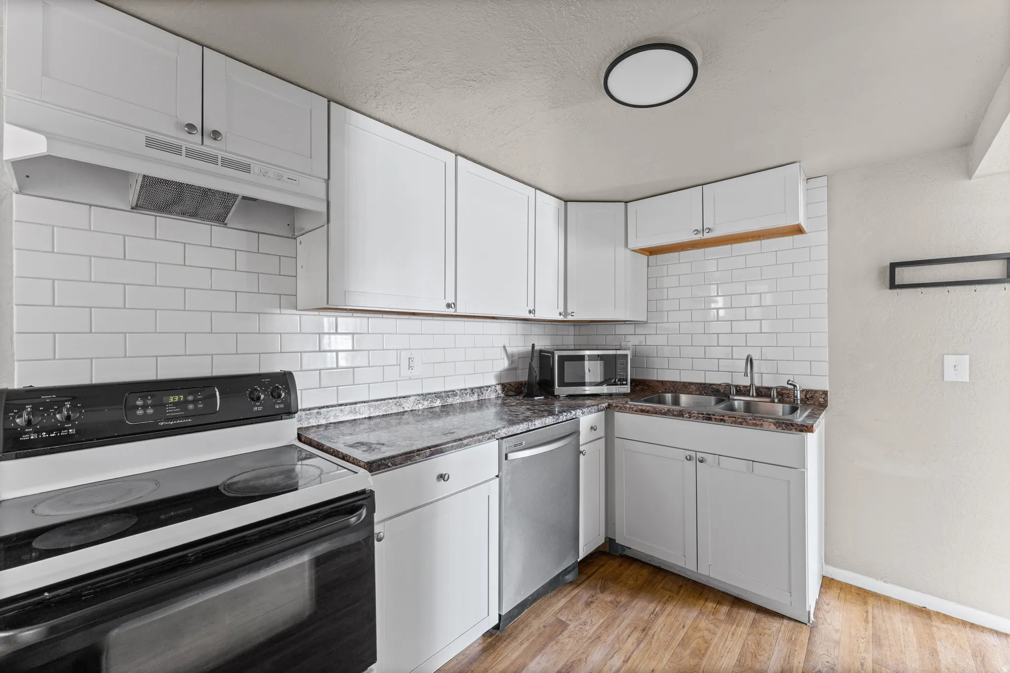 Kitchen featuring white cabinetry, subway tile backsplash, laminate countertops, stainless steel dishwasher, and wood-finish flooring