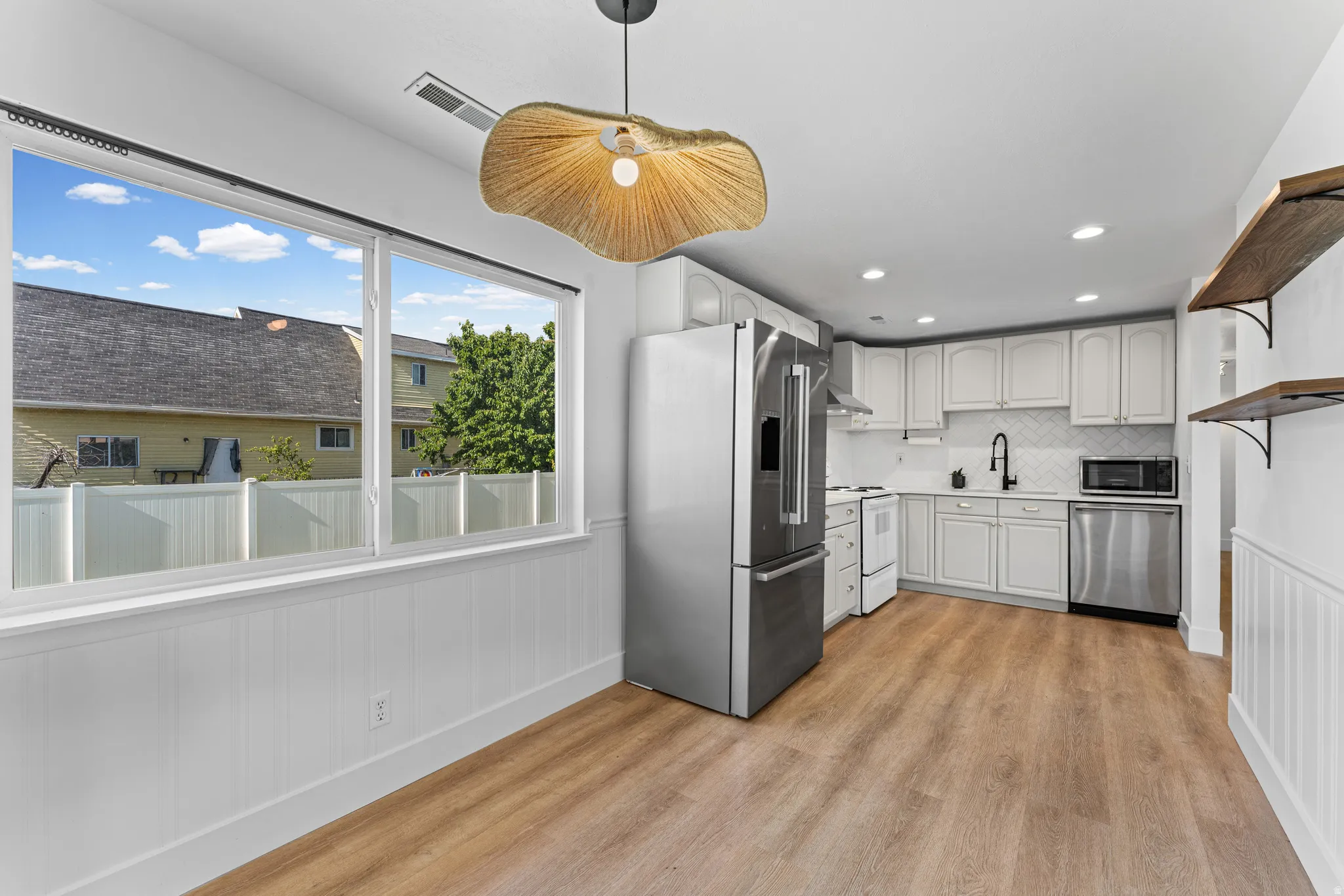 Kitchen and dining area featuring wood-finish flooring, white wainscoting, and a decorative pendant light fixture
