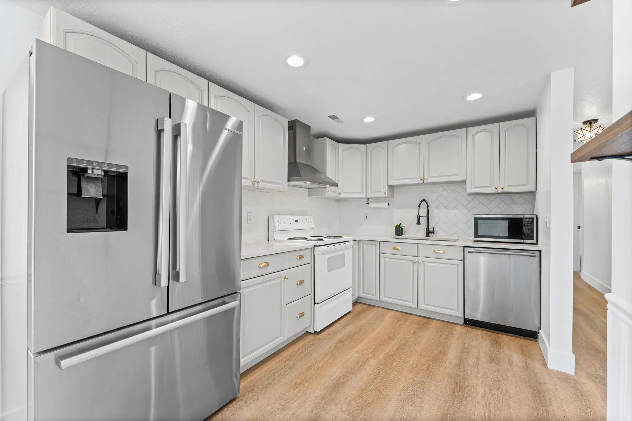 Contemporary kitchen featuring light wood-finish flooring, white cabinetry with gold-tone hardware, and stainless steel appliances