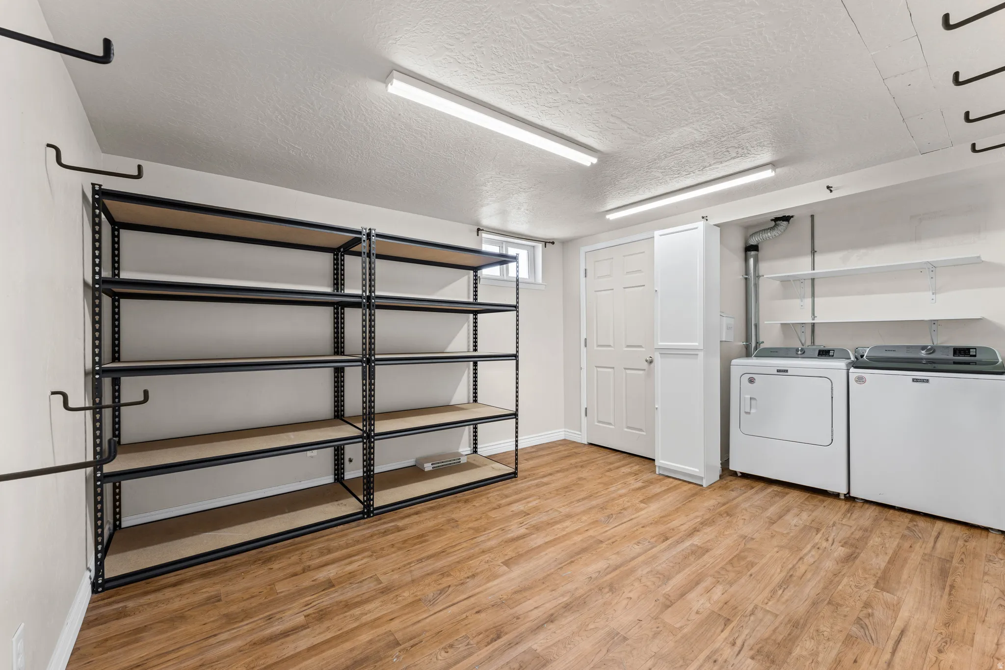 Utility room featuring wood-finish flooring, fluorescent lighting, built-in shelving, white paneled door, and a tall white storage cabinet