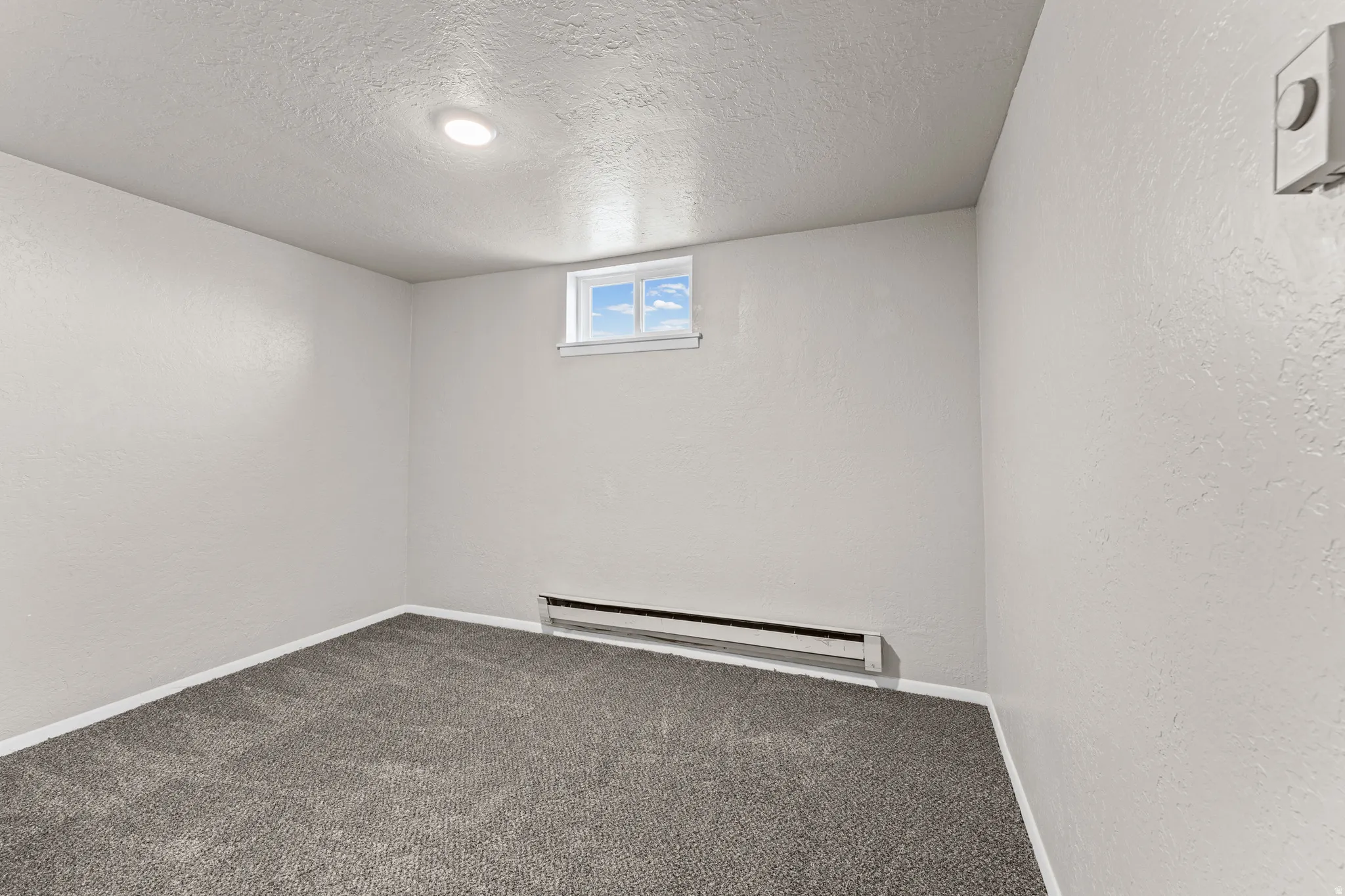 Neutral painted walls with a textured finish, grey carpet flooring, and white baseboards