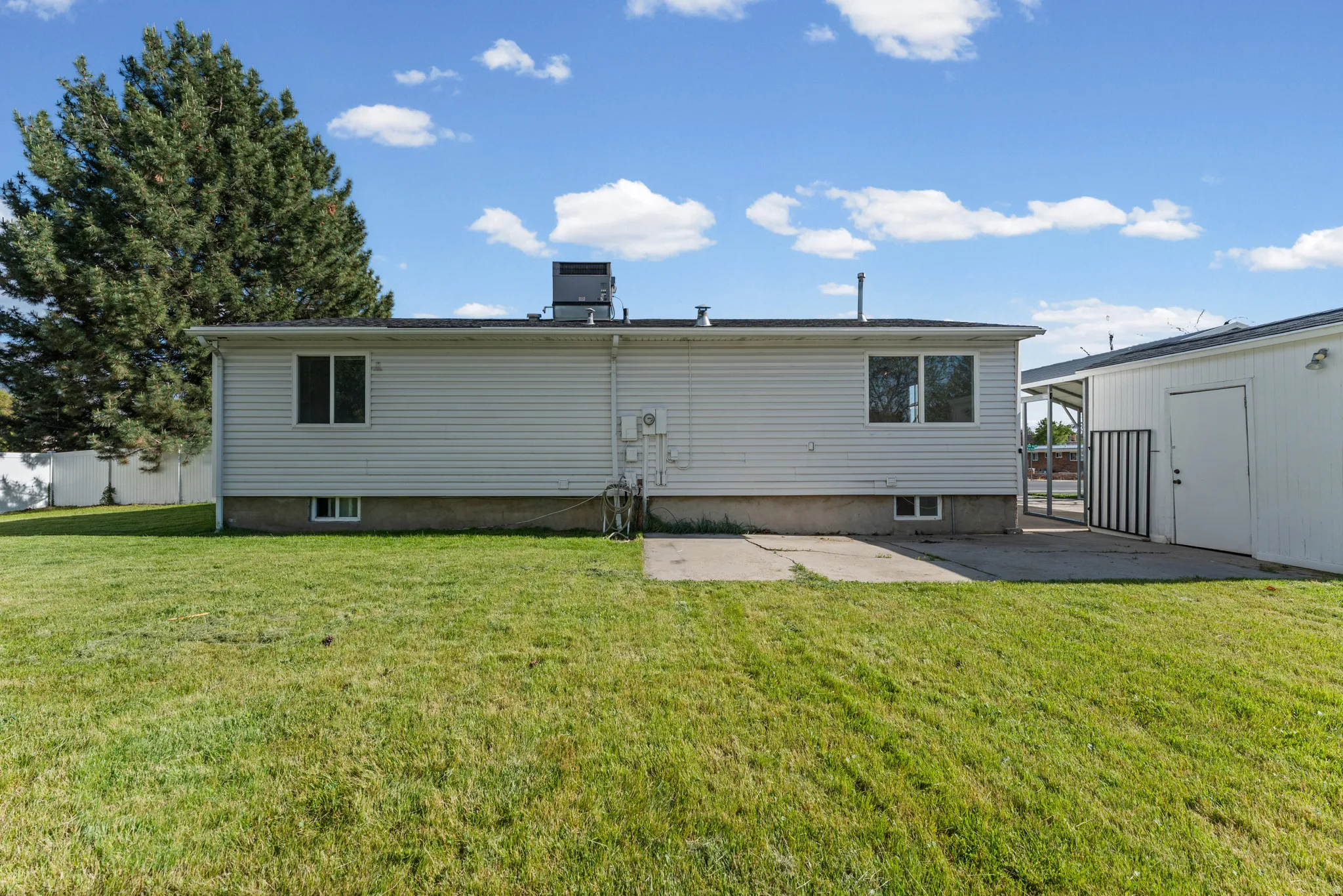 Expansive green lawn surrounding a white vinyl-sided structure with multiple windows and a concrete patio