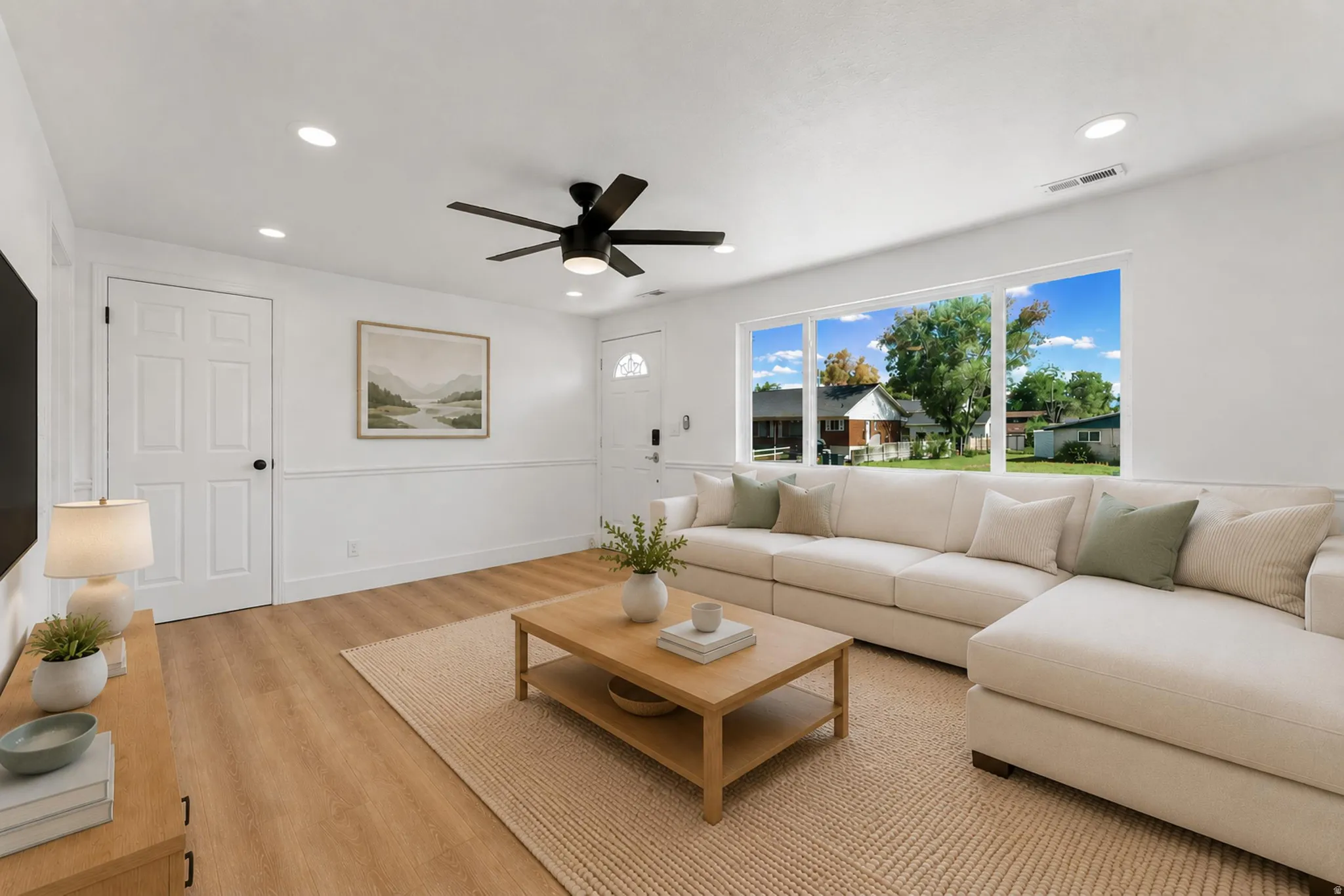 Bright living space featuring wood-finish flooring, white walls with wainscoting, recessed lighting, and a multi-pane window