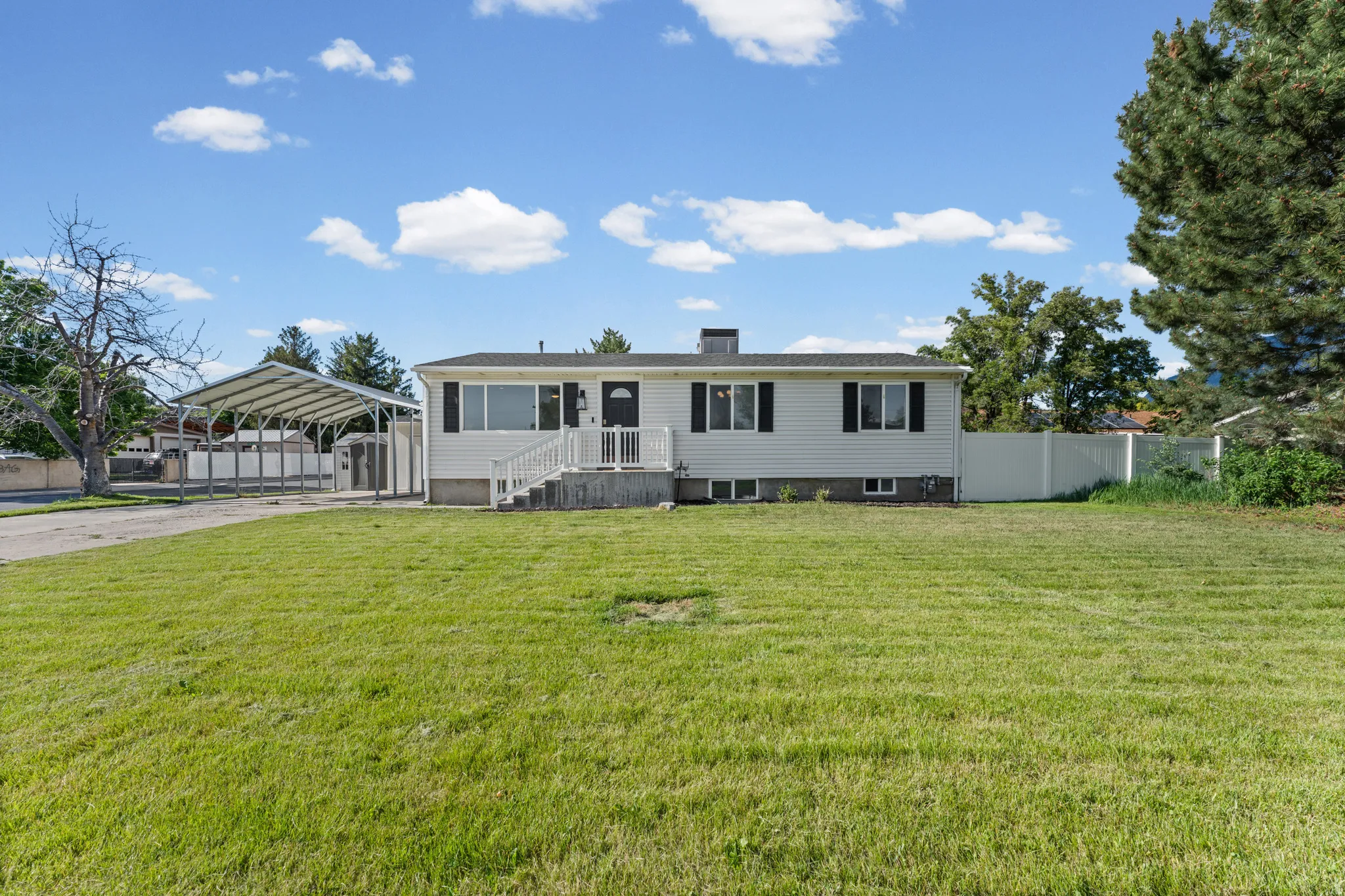 White exterior home with black shutters, a covered porch entry, and a multi-car carport