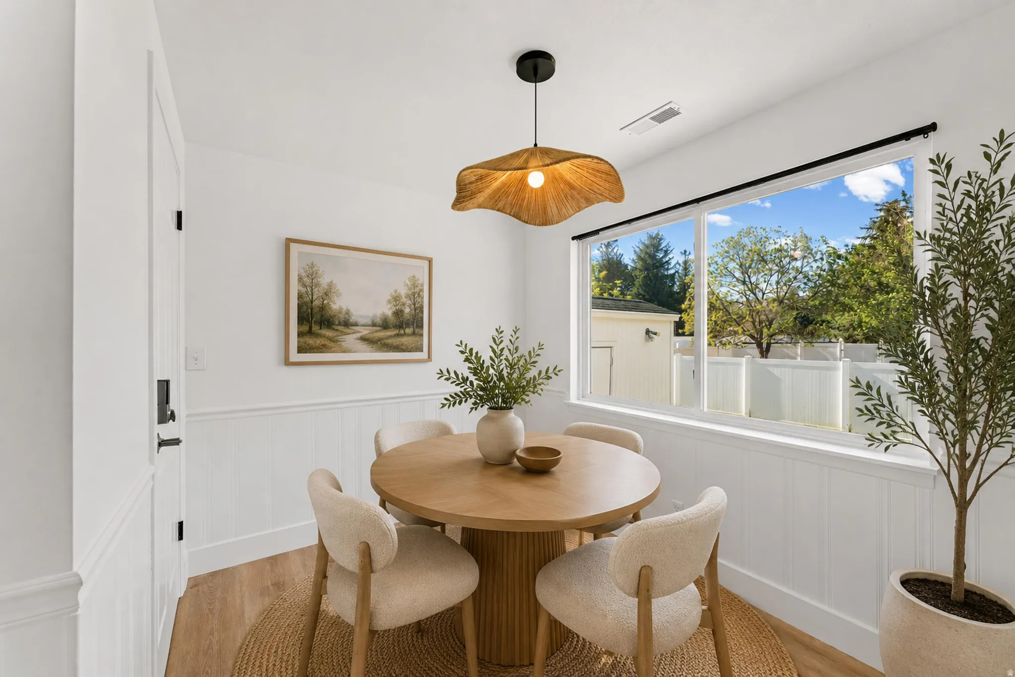 Dining area featuring wood-finish flooring, white wainscoting, and a large picture window