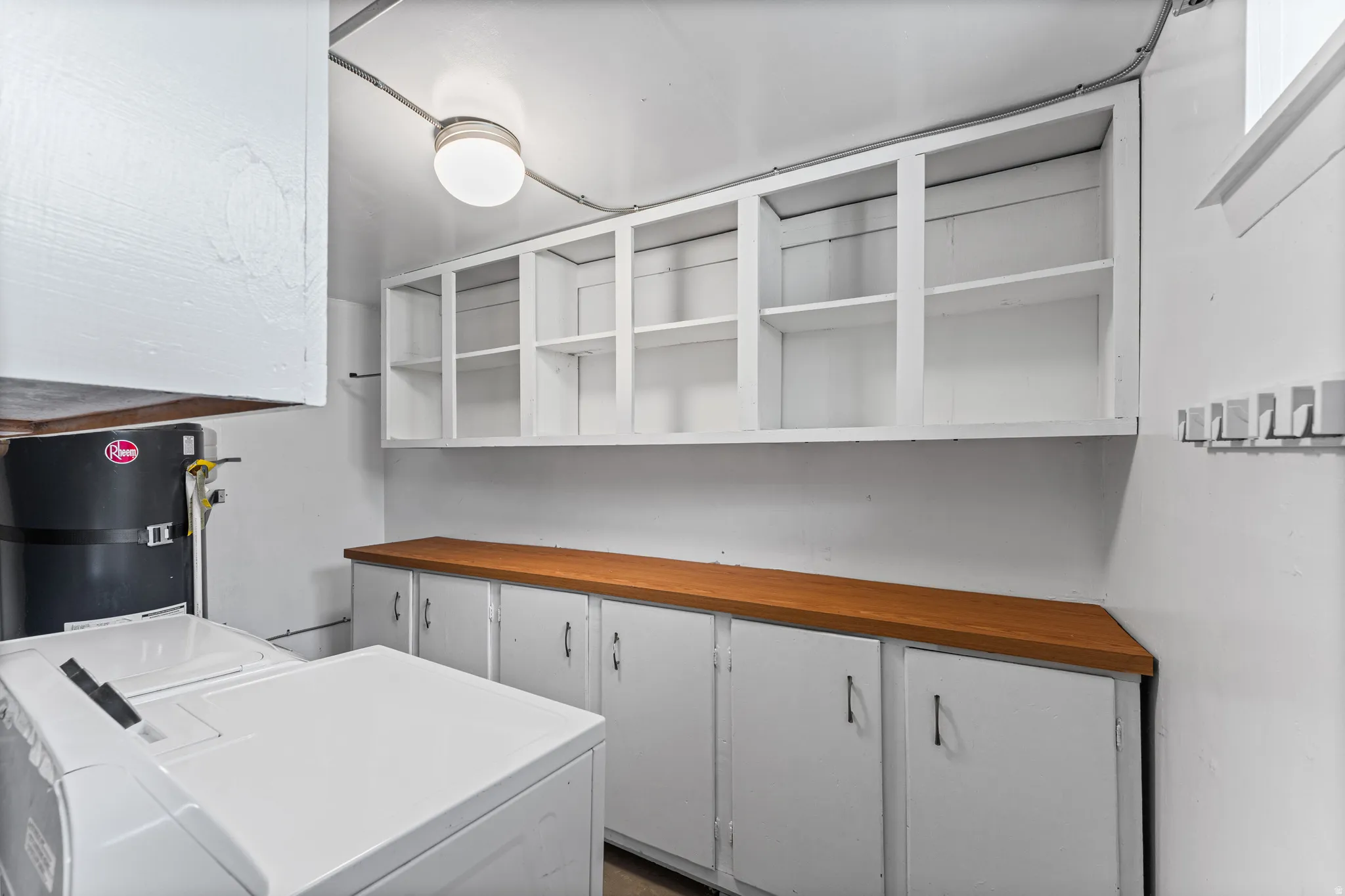 Utility room featuring white shaker-style cabinetry, wood-finish countertops, overhead open shelving, and a ceiling-mounted light fixture