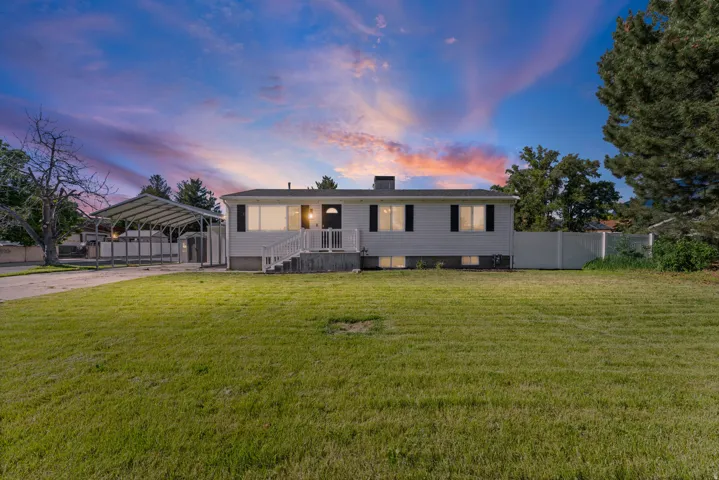 Ranch-style residence featuring white siding, black shutters, a covered front porch with white railings, a large front lawn, and a multi-car carport