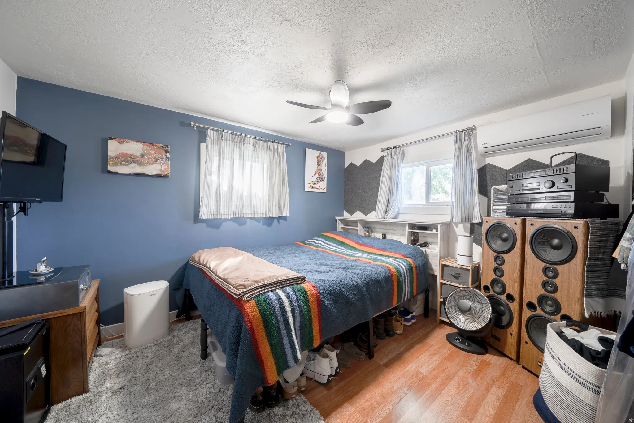 Bedroom featuring wood-finish flooring, a ceiling fan, and a wall-mounted climate control unit