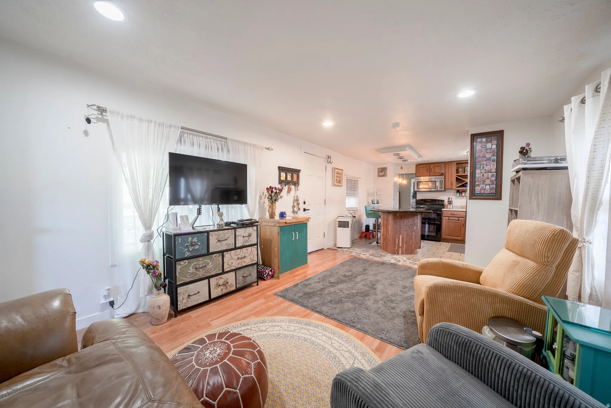 Open-concept living space featuring wood-finish flooring, recessed lighting, and a kitchen with warm wood cabinetry, a black range, and an integrated microwave