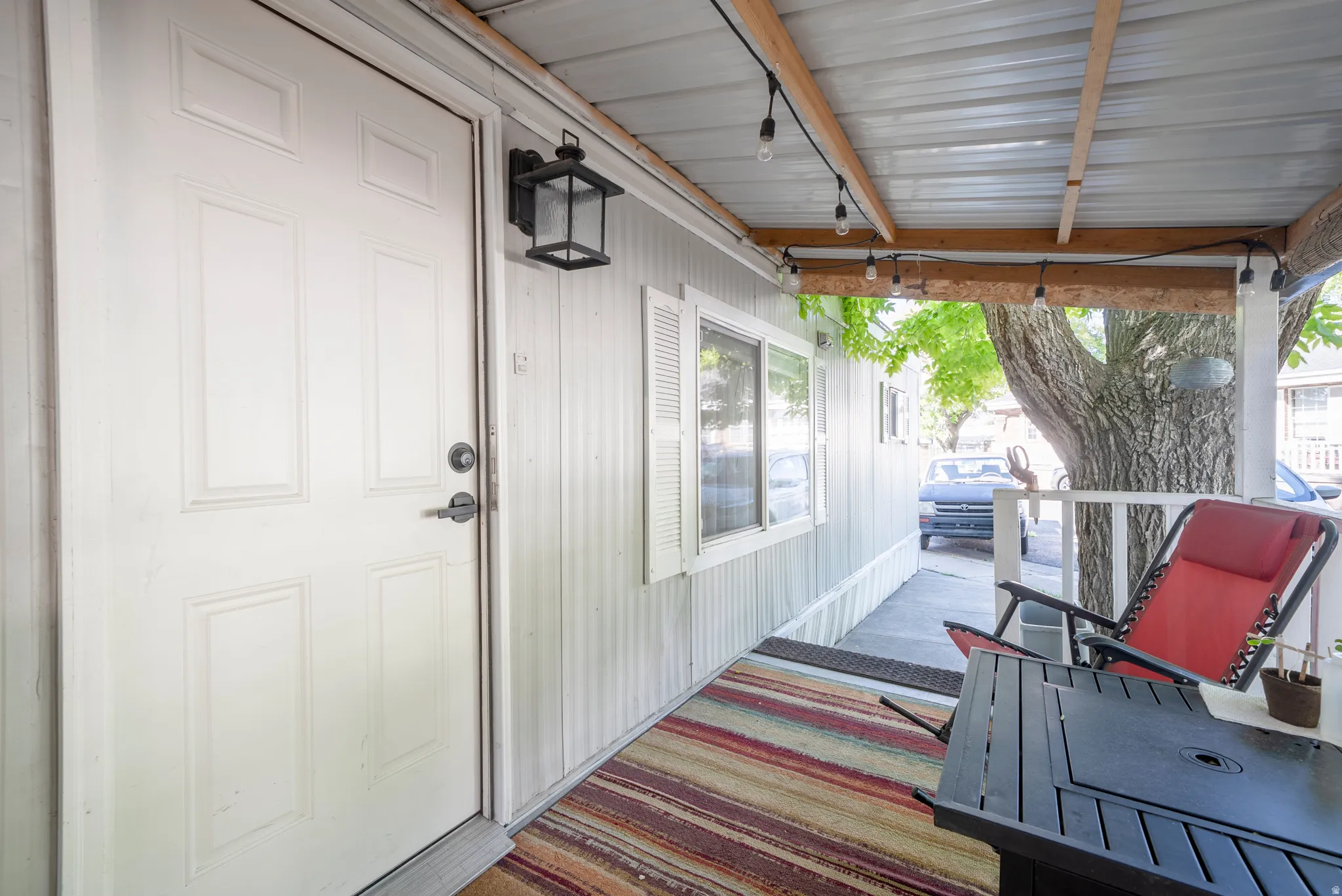 Covered front porch featuring a paneled entry door, exterior wall lantern, white siding, and a metal roof
