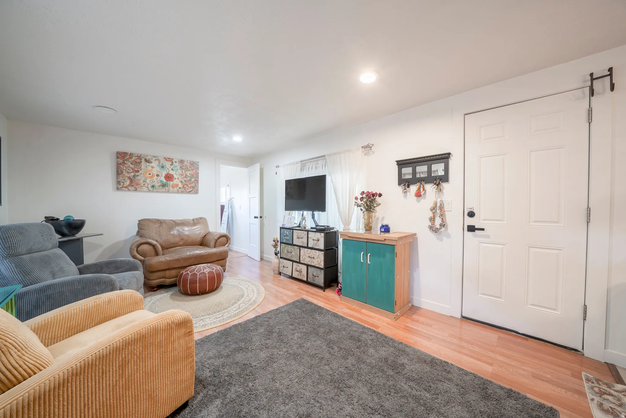 Living area featuring wood-finish flooring, white walls, recessed lighting, and a paneled entry door with black hardware