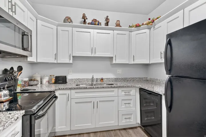 Modern kitchen featuring white shaker cabinetry, granite-style countertops, stainless steel microwave, black electric range, and black refrigerator