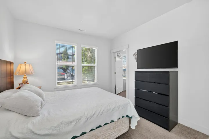 Bedroom featuring two windows with blinds, a wood-finish headboard, and light-toned carpeting