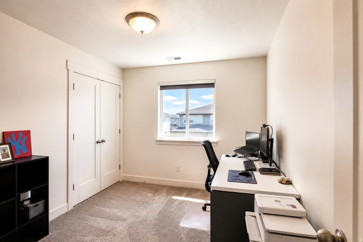 Room featuring a window with a roller shade, light neutral wall paint, and a textured carpeted floor