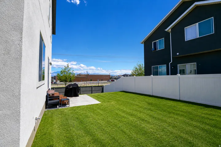 Expansive green lawn featuring a concrete patio, white vinyl fencing, and a two-story exterior with multiple windows