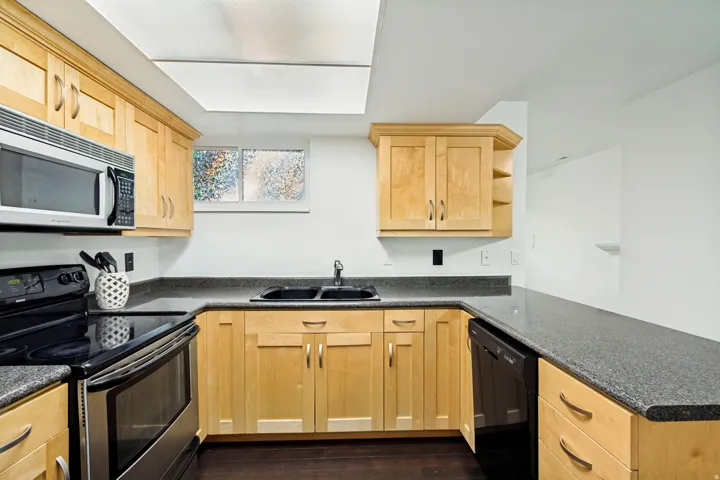 U-shaped kitchen featuring wood cabinetry, dark countertops, a black double basin sink, stainless steel microwave, and a black and stainless steel range